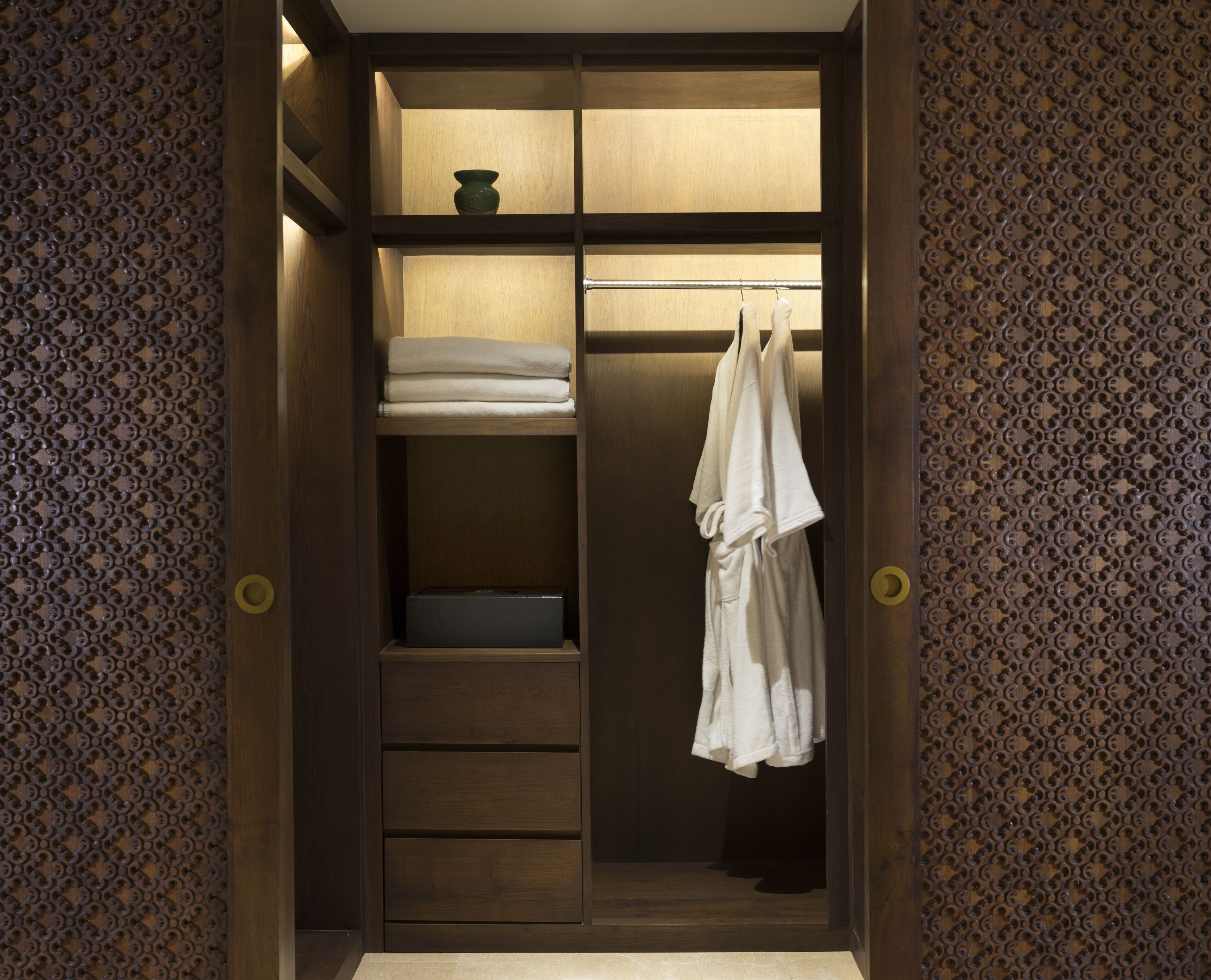 A walk-in closet with wooden shelves, a hanging robe, and a small vase.