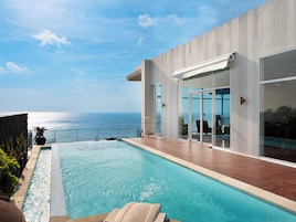 A modern poolside area with a view of the sea, a glass-enclosed patio, and a wooden deck.