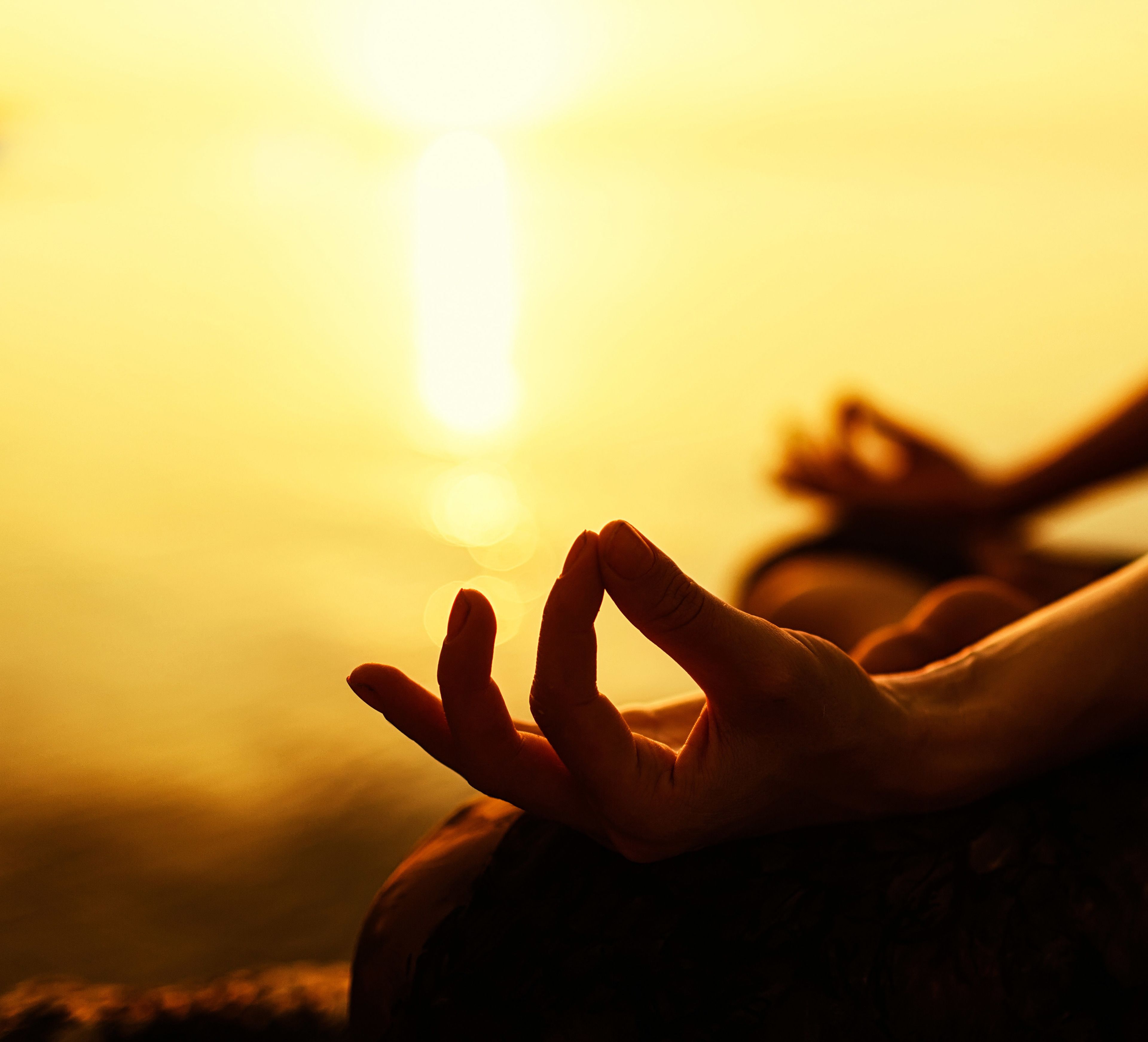 Una persona meditant amb el sol ponent al fons.