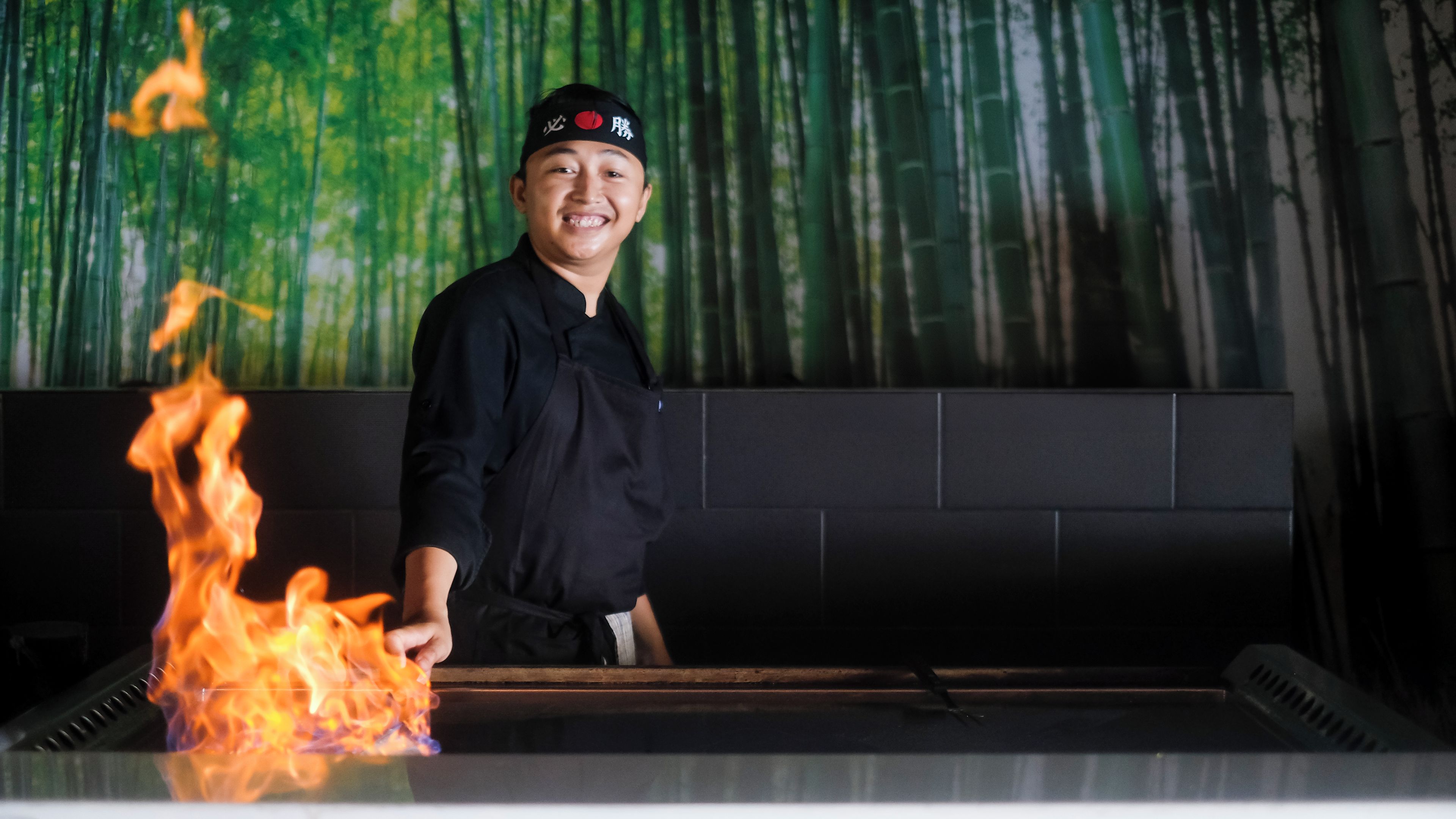 A chef standing in front of a cooking station with flames.