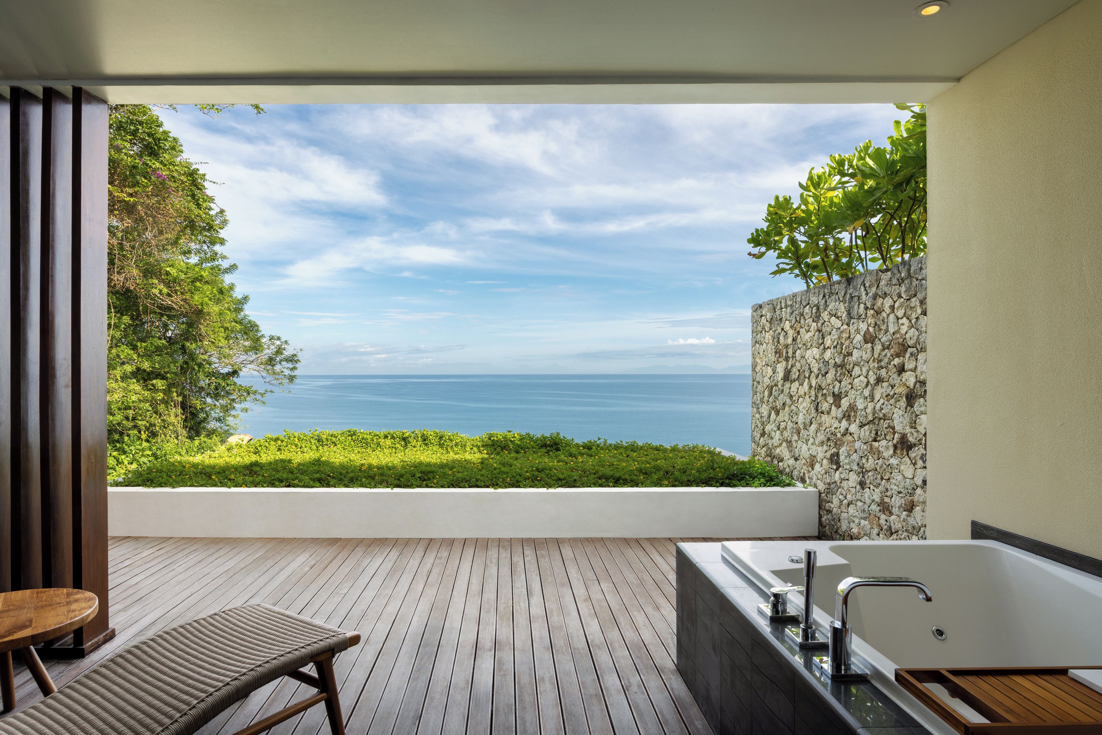 A modern bathroom with a bathtub, a wooden bench, and a view of the sea.