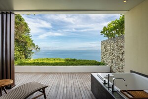 A modern bathroom with a bathtub, a wooden bench, and a view of the sea.
