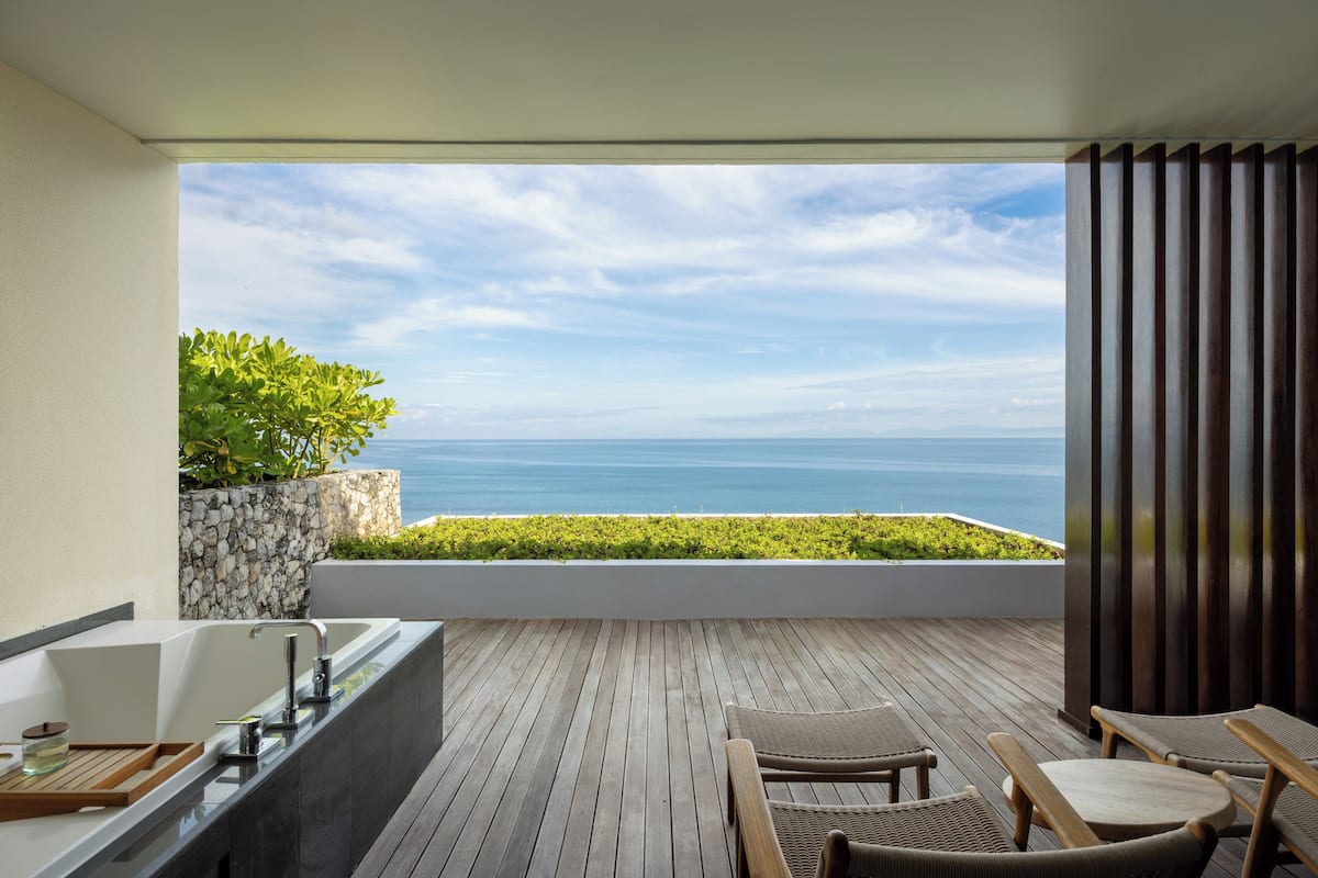 A balcony with a wooden floor, a built-in bathtub, and a seating area with two chairs.