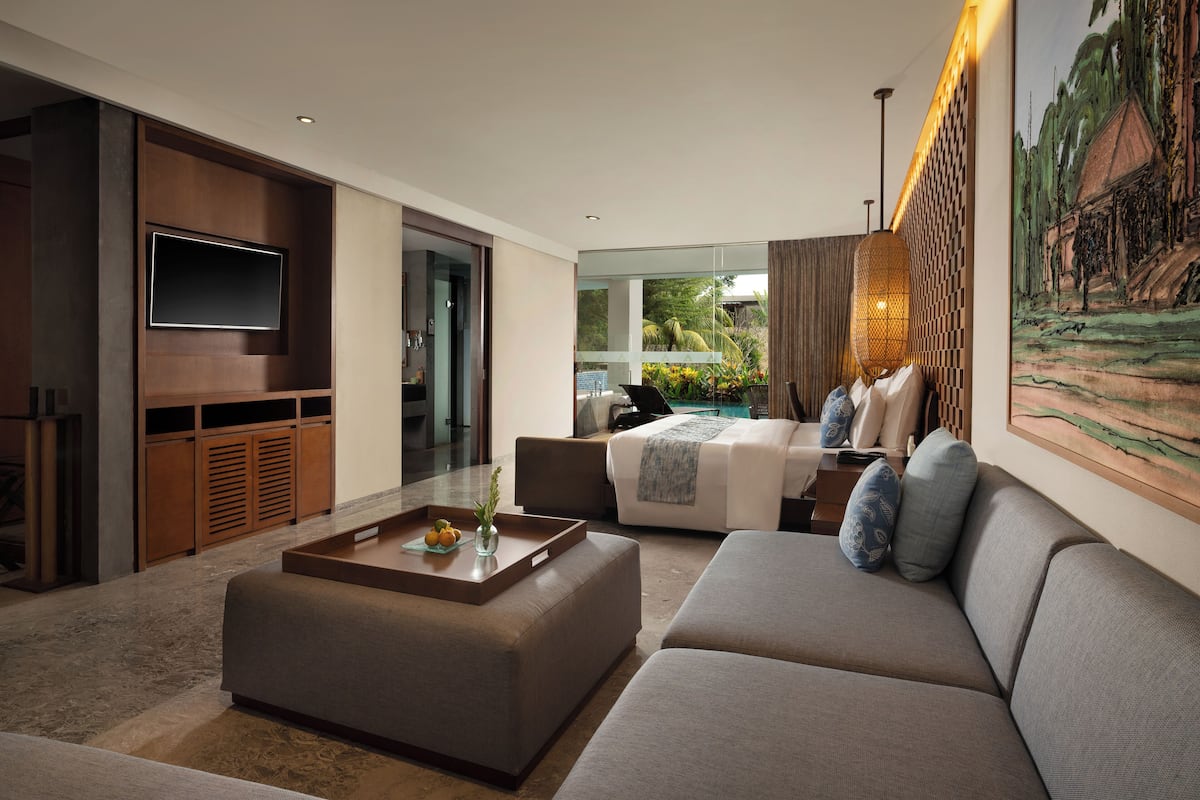 A modern hotel room with a large bed, a sofa, a coffee table, and a TV mounted on the wall.