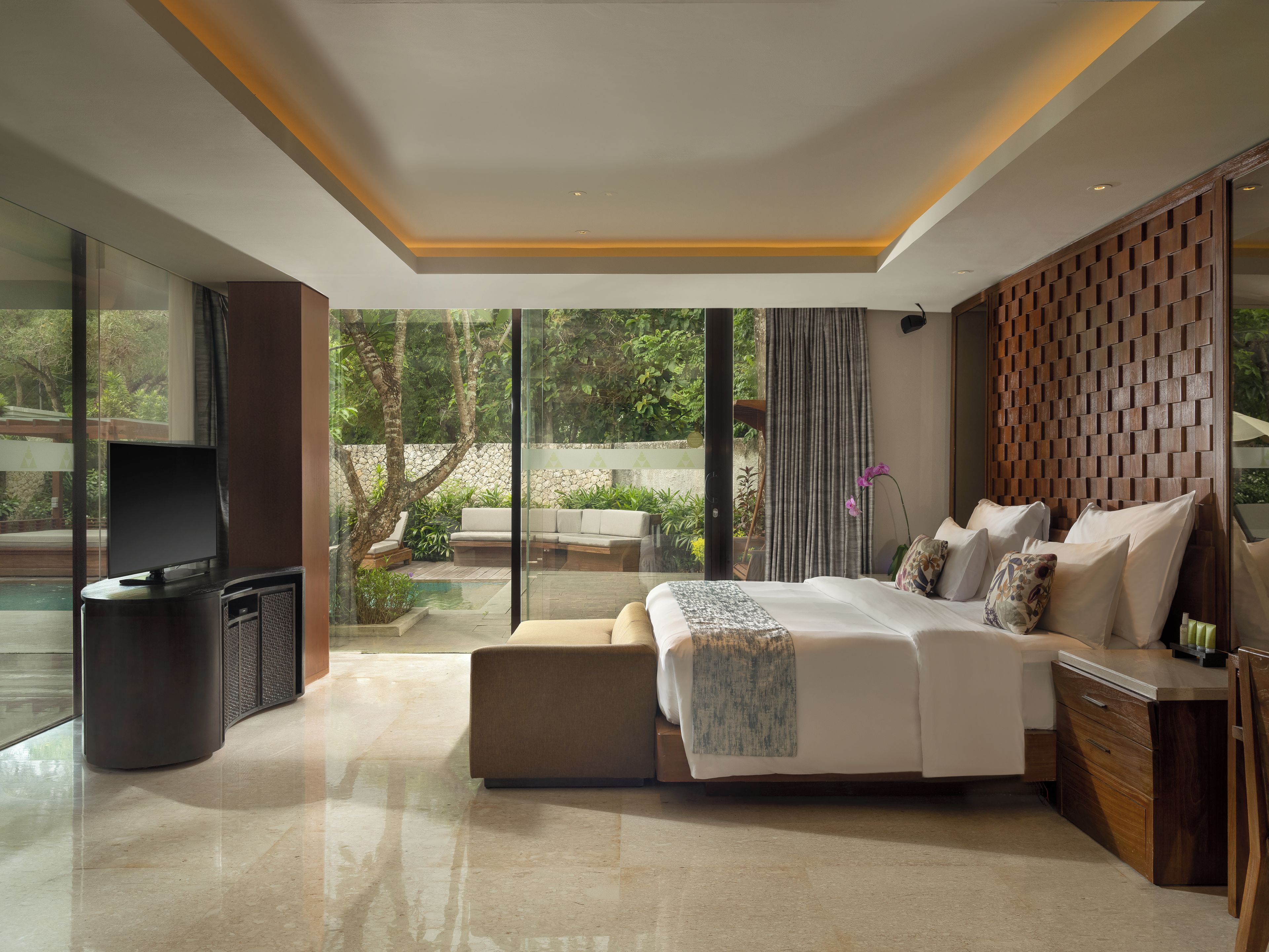 A modern bedroom with a large bed, a TV, and a view of a garden.