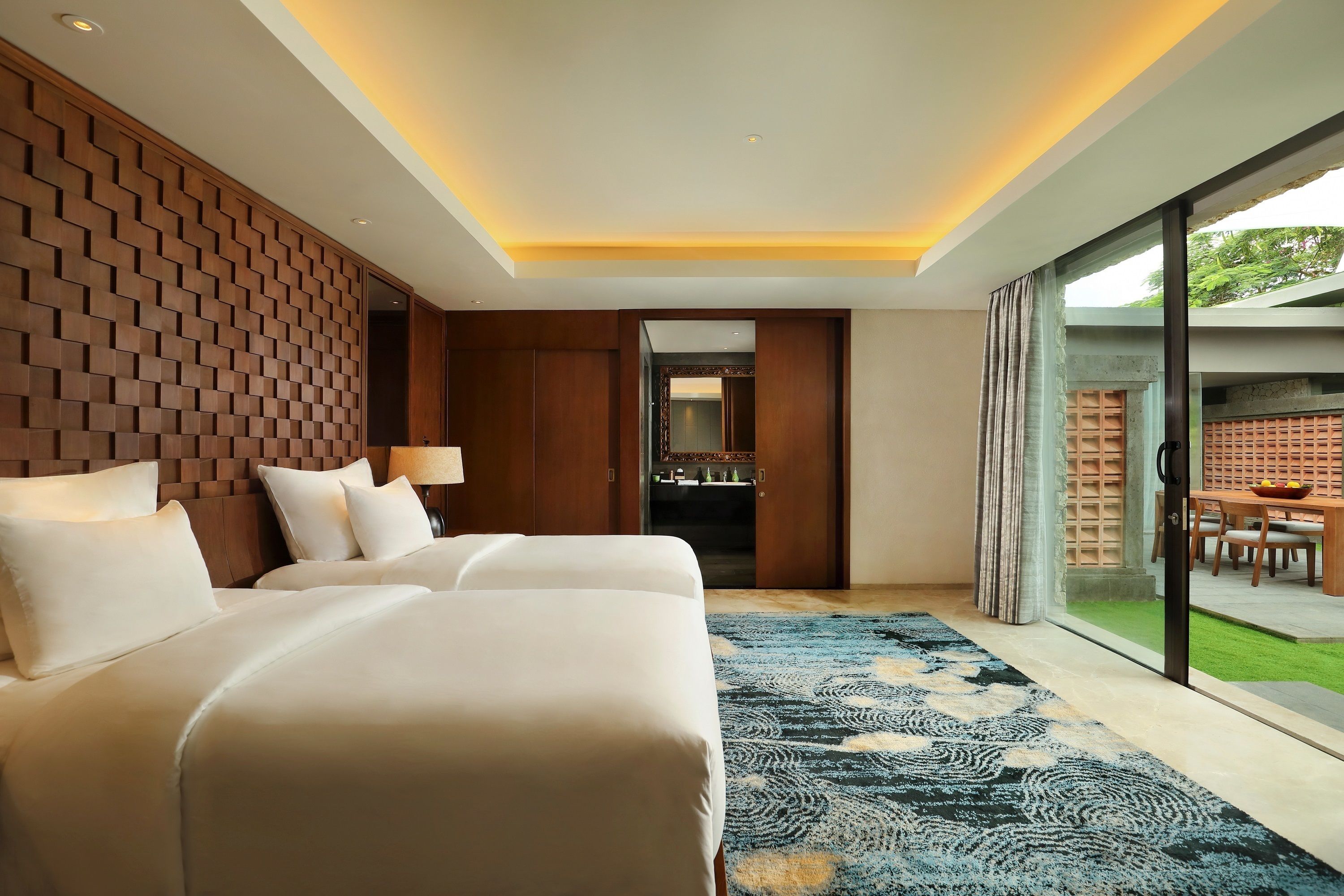 A modern hotel room with a large bed, a wooden accent wall, and a view of the outdoor area.