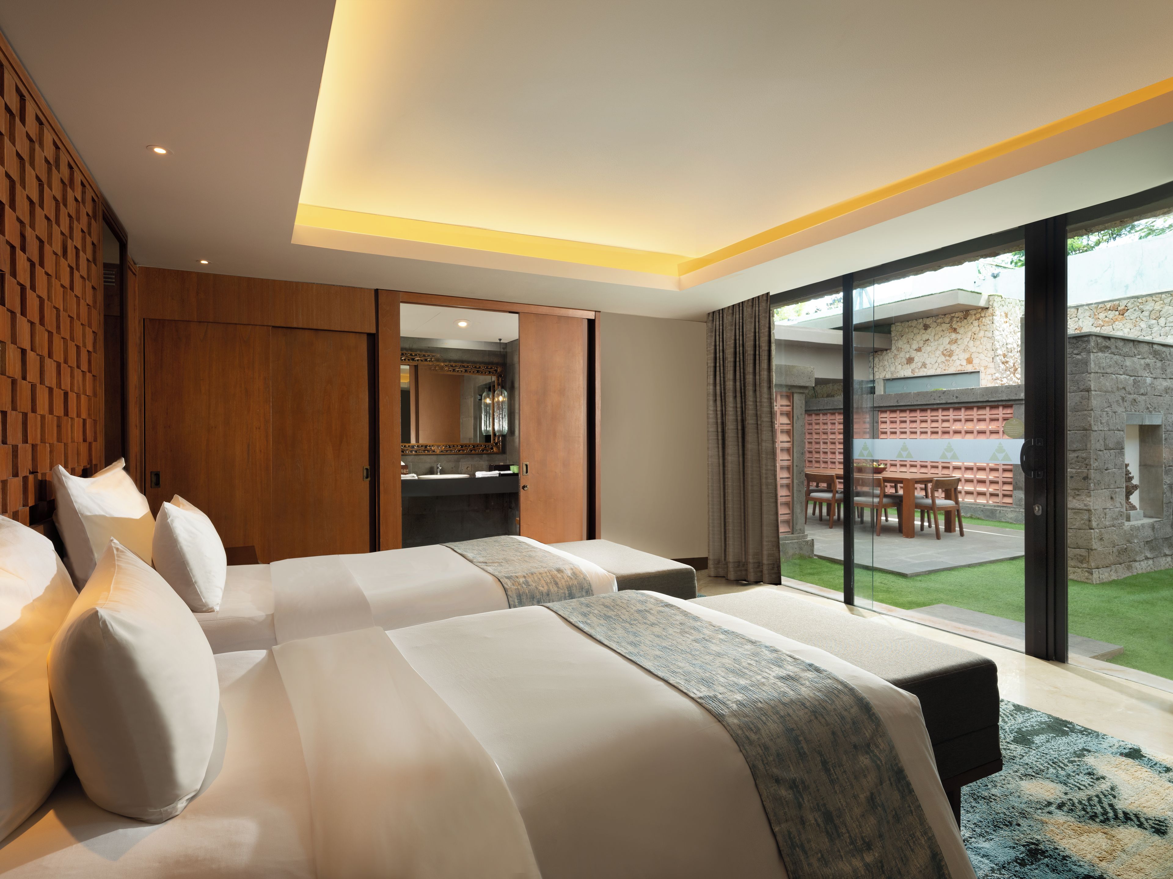 Habitación de hotel con dos camas, un baño y vista a un patio exterior.