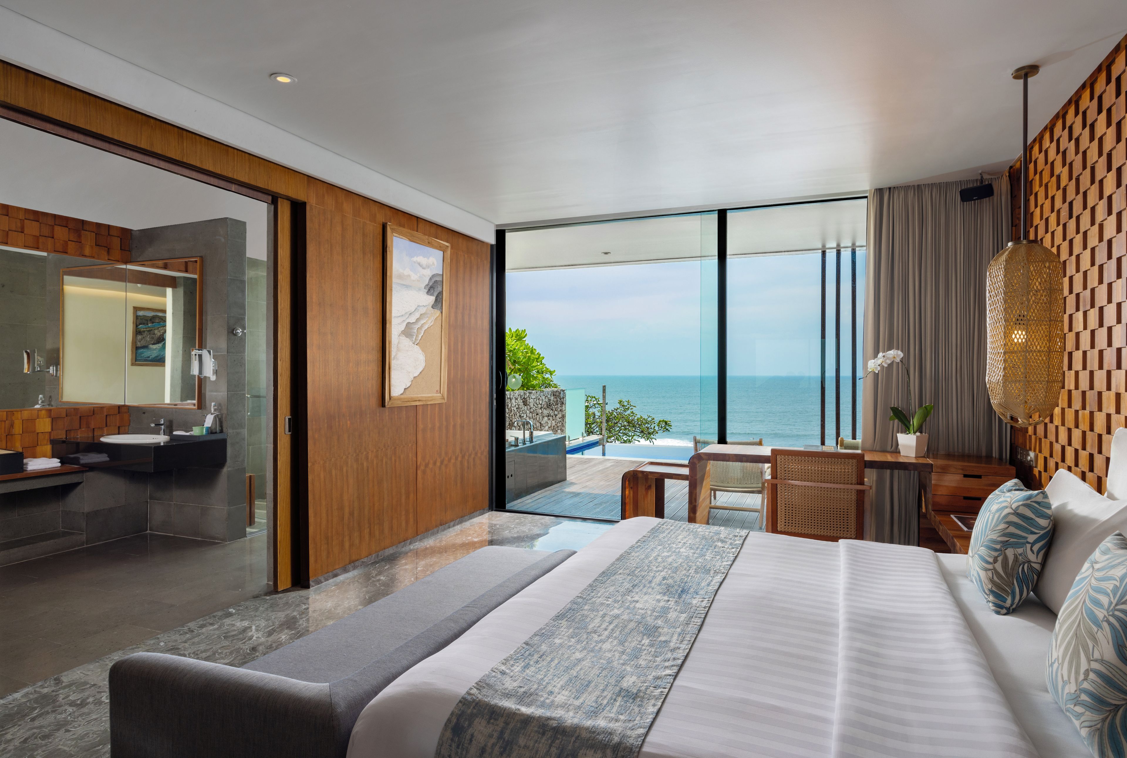 A modern hotel room with a large bed, a bathroom with a mirror and sink, and a view of the sea.