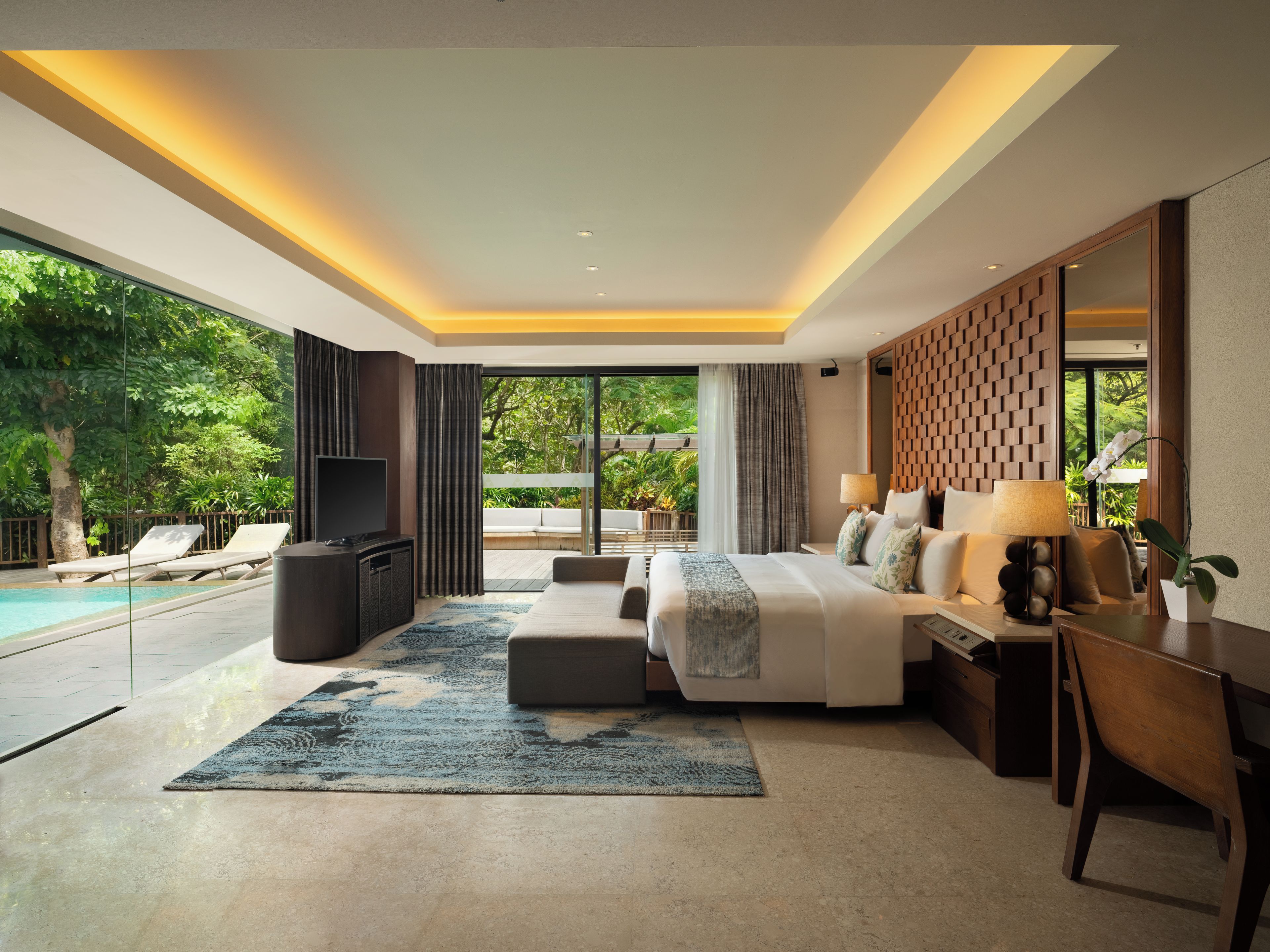 A modern hotel room with a large bed, a desk, a TV, and a view of a swimming pool and greenery.