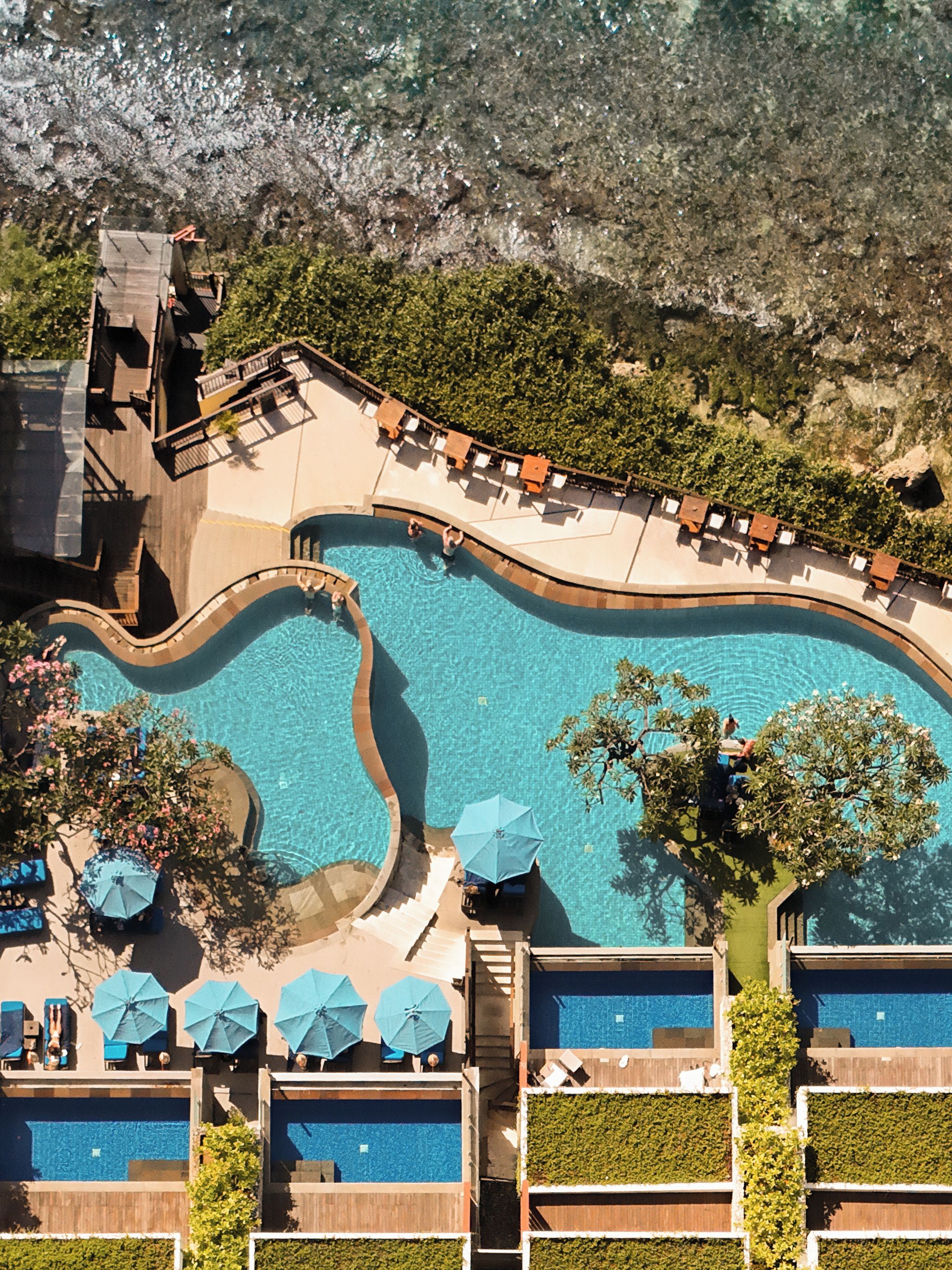 An aerial view of a resort with a large swimming pool, sun loungers, and a landscaped area.