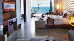 A modern hotel room with a large bed, a seating area, and a TV mounted on the wall. - Anantara Uluwatu Bali Resort (Pecatu)