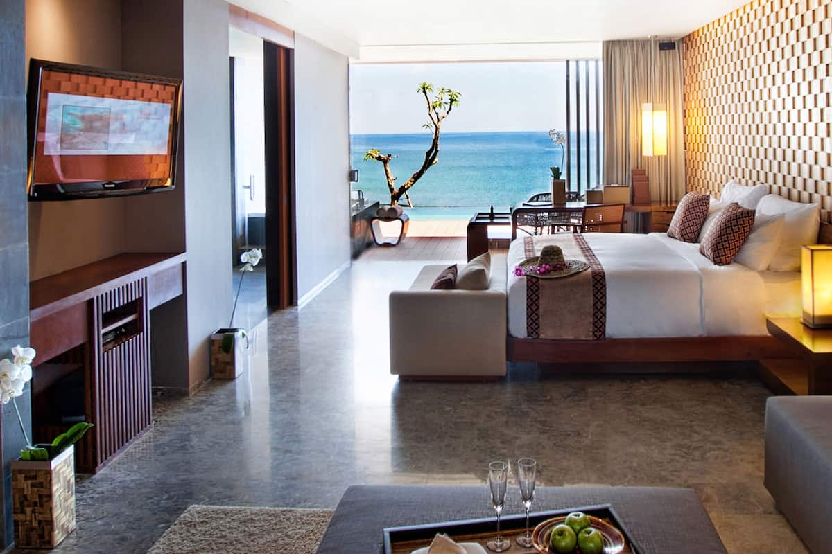 A modern hotel room with a large bed, a seating area, and a TV mounted on the wall.