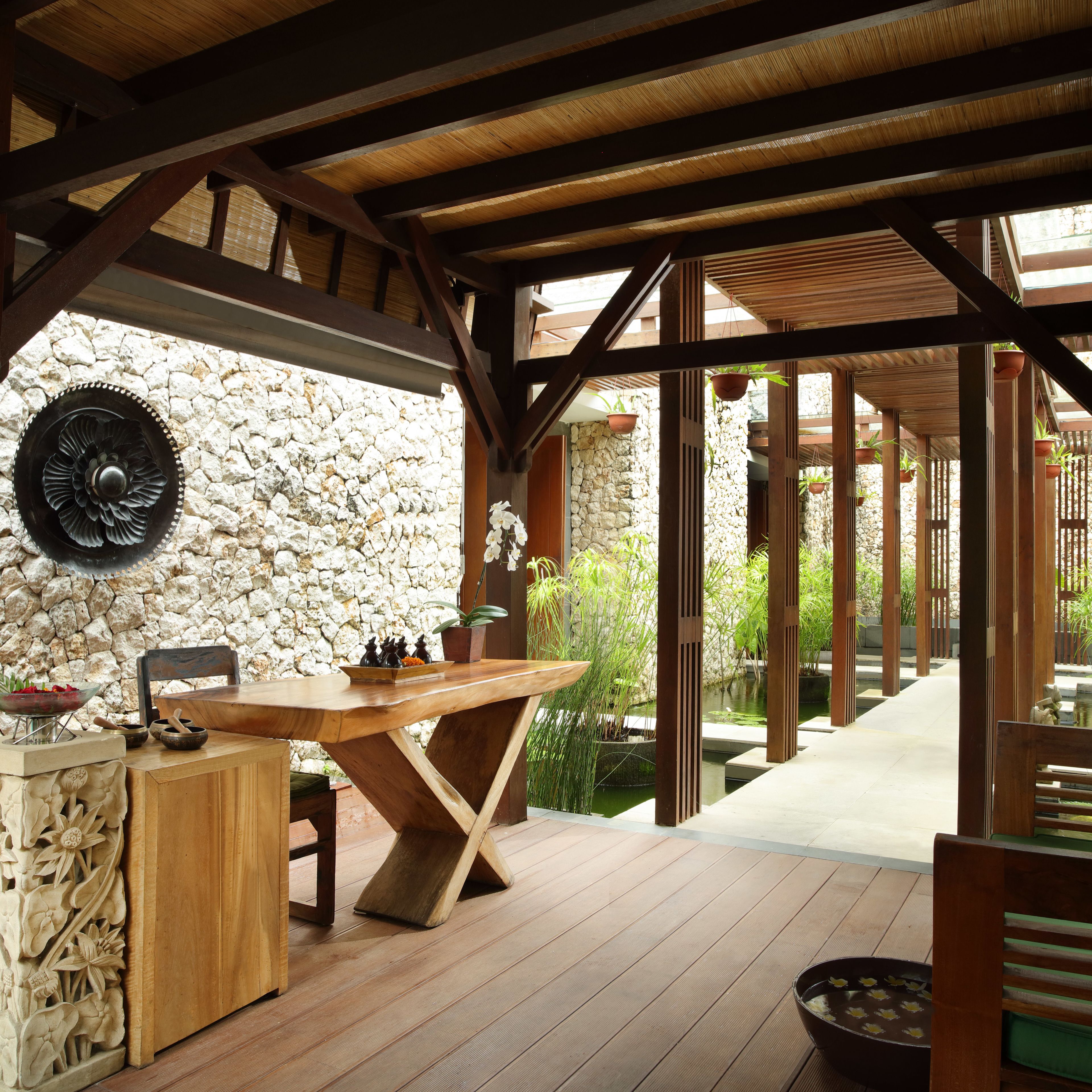 Une terrasse en bois avec un muret en pierre, une table sur laquelle se trouve un saladier rempli de fruits et des plantes en pot.