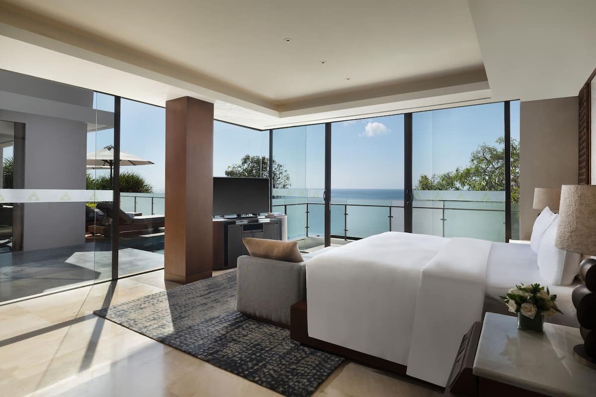 A modern hotel room with a large bed, a seating area with a view, and a balcony with a glass railing.