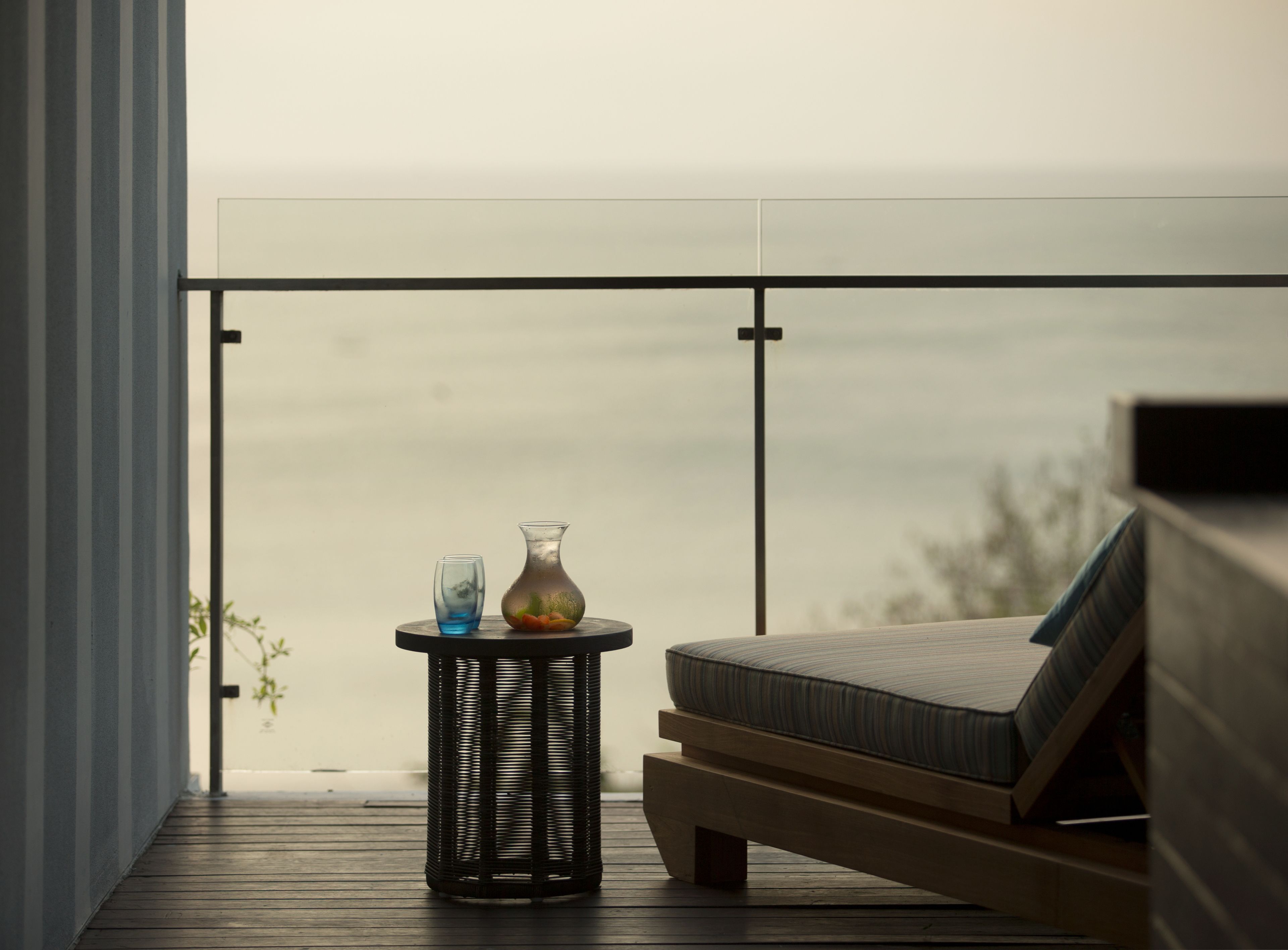 A balcony with a wicker table, a vase with flowers, and a cushioned seating area.
