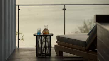 A balcony with a wicker table, a vase with flowers, and a cushioned seating area.