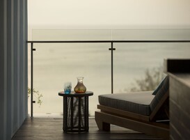 A balcony with a wicker table, a vase with flowers, and a cushioned seating area.