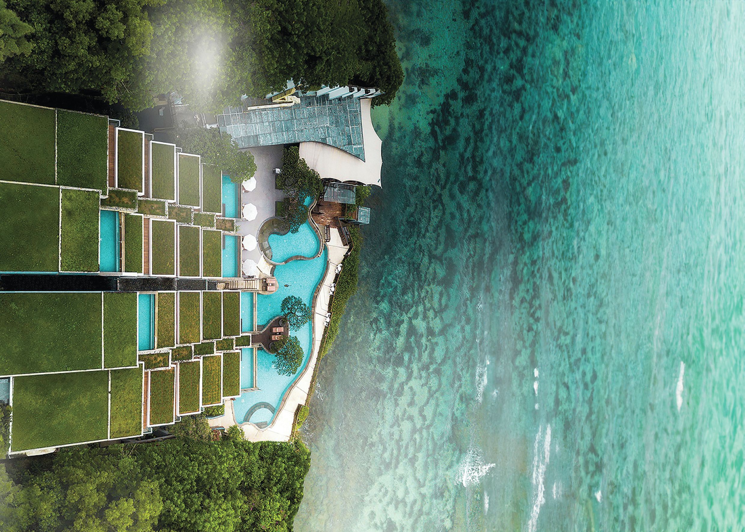 Vista aérea de um resort com piscina, áreas de descanso e uma grande extensão de água.