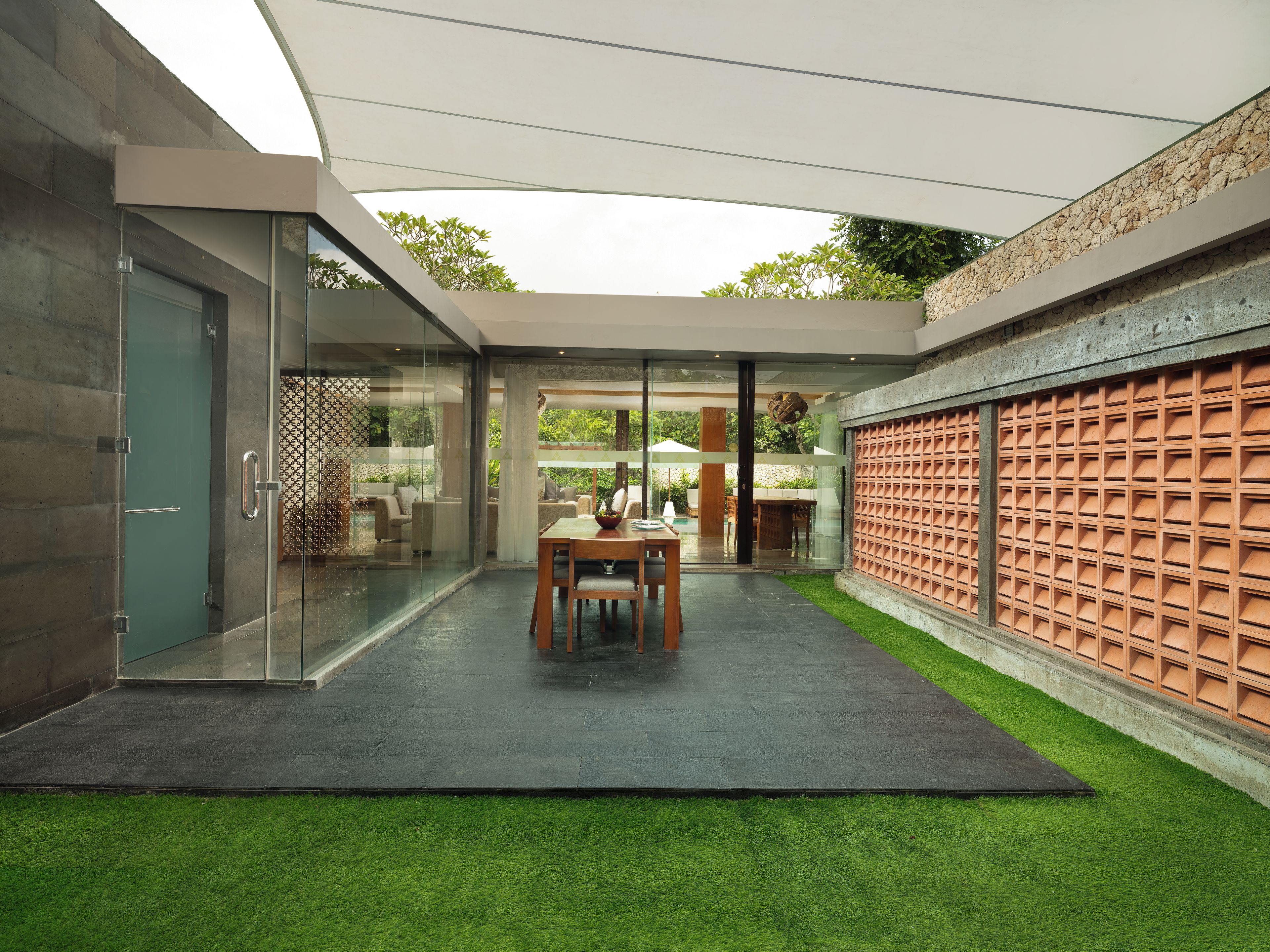 Un patio moderno al aire libre con una mesa de comedor, sillas y un ventanal de vidrio que da a un jardín.