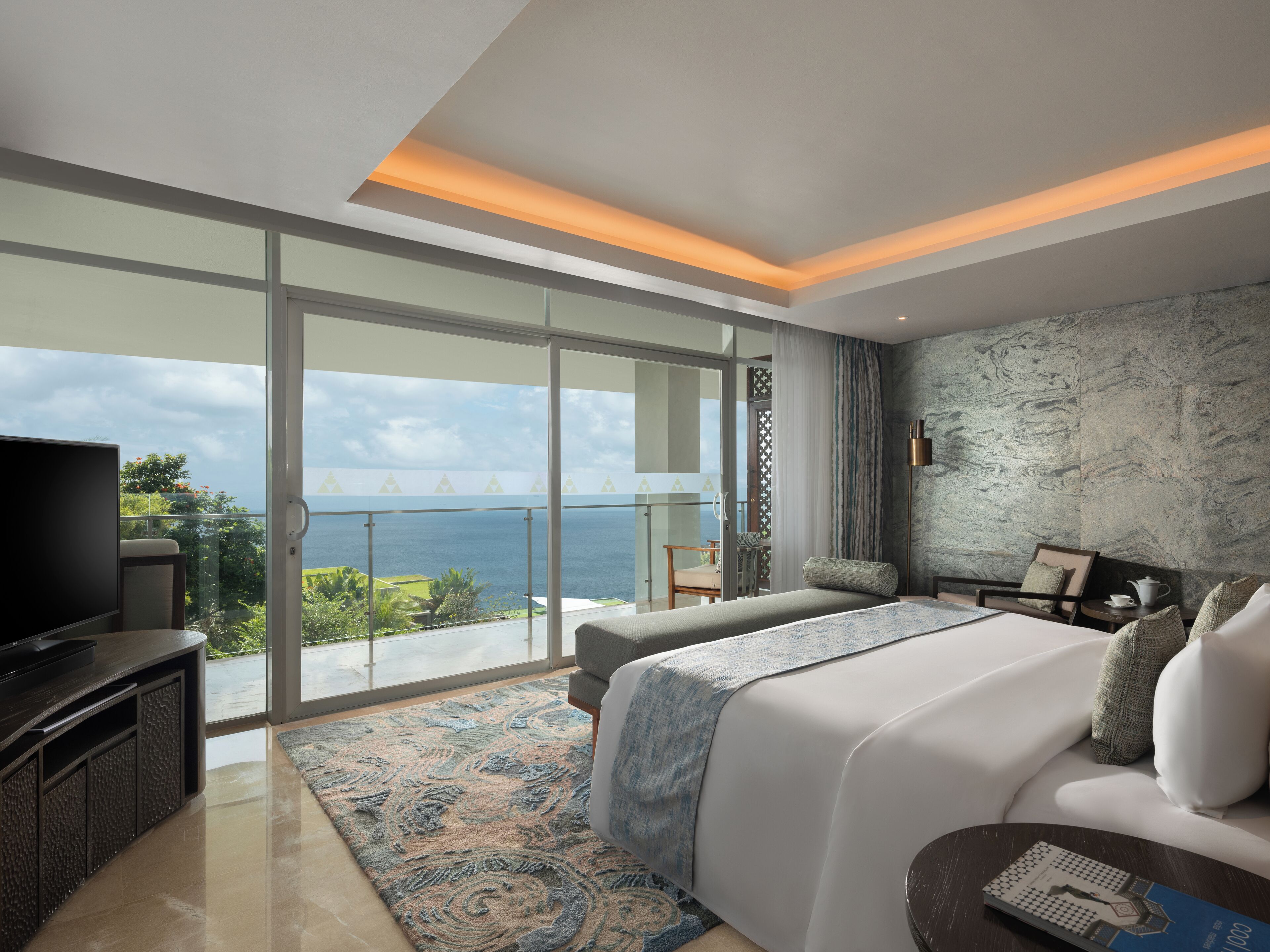 Ein modernes Hotelzimmer mit großem Balkon, einem Flachbildfernseher, einem Bett mit gemustertem Teppich und einer Wand mit Steinoptik.