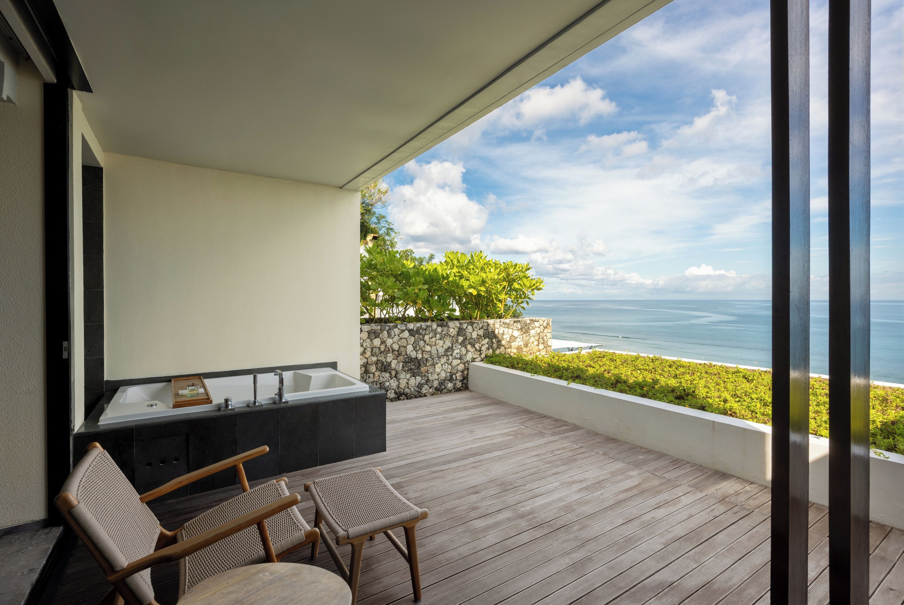A balcony with a wooden floor, a stone wall, and a view of the ocean.