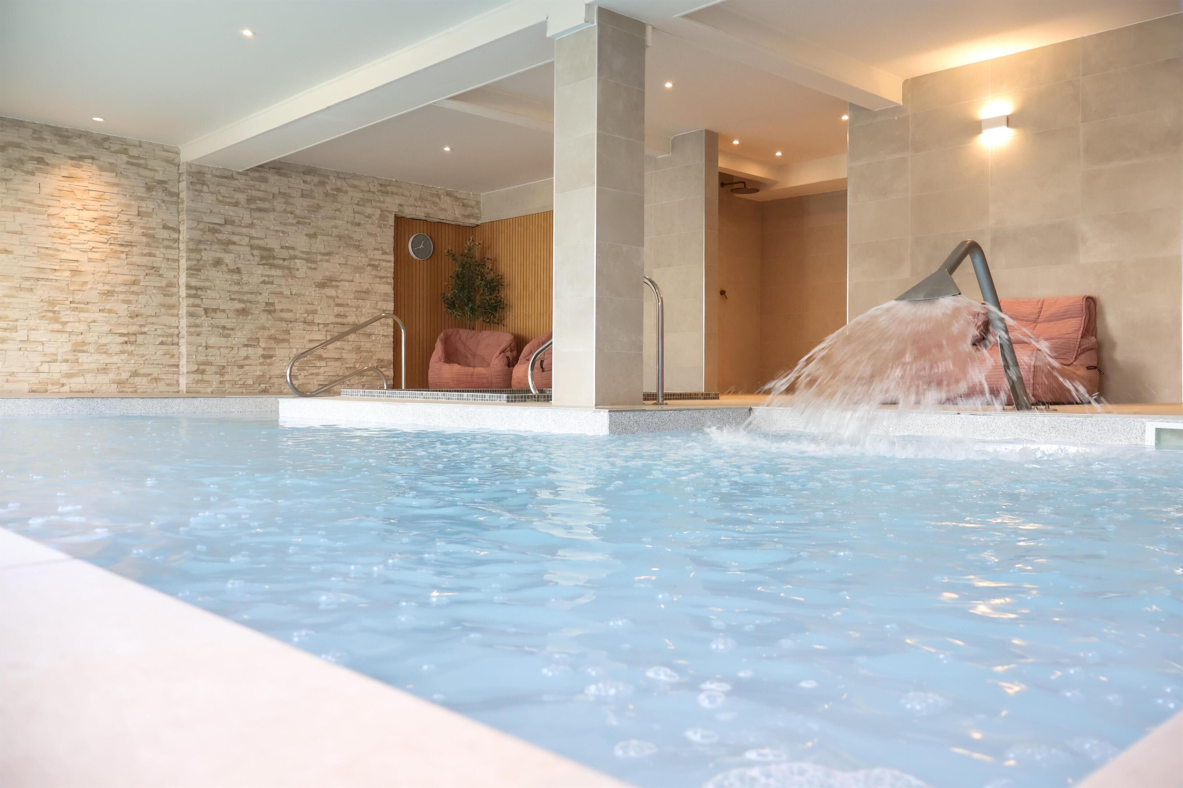 An indoor swimming pool with a stone wall, a clock, and a chair.