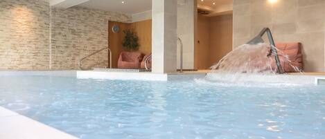 An indoor swimming pool with a stone wall, a clock, and a chair.