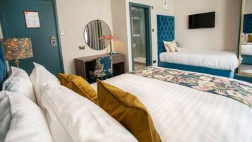 A hotel room with a large bed, a smaller bed, a TV, a mirror, a door, and a bathroom visible through an open door.