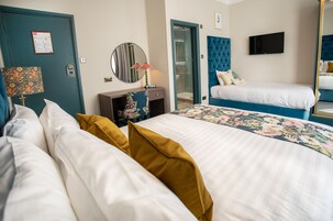 A hotel room with a large bed, a smaller bed, a TV, a mirror, a door, and a bathroom visible through an open door.