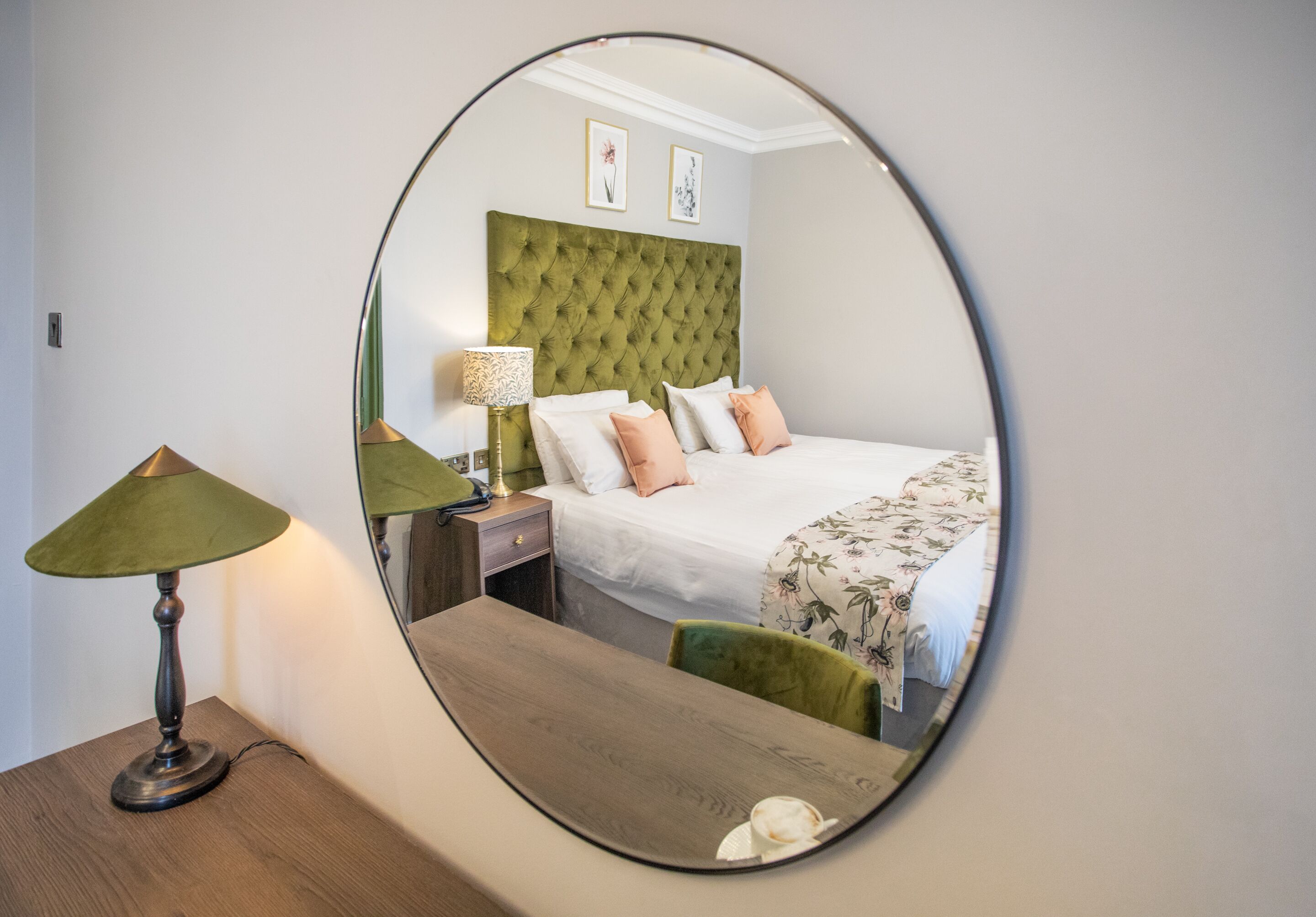 Une chambre à coucher avec un miroir rond, un lit avec une literie à motifs floraux, une table de chevet et une lampe.