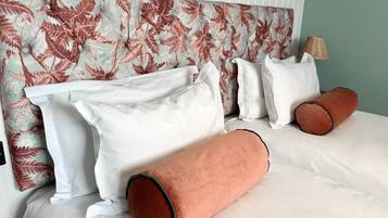 A neatly made bed with white linens and two orange pillows, a white headboard with a leafy pattern, and a lamp on the side.