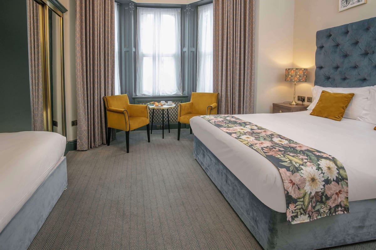 A hotel room with a large bed, a smaller bed, a table with chairs, and a window with curtains.