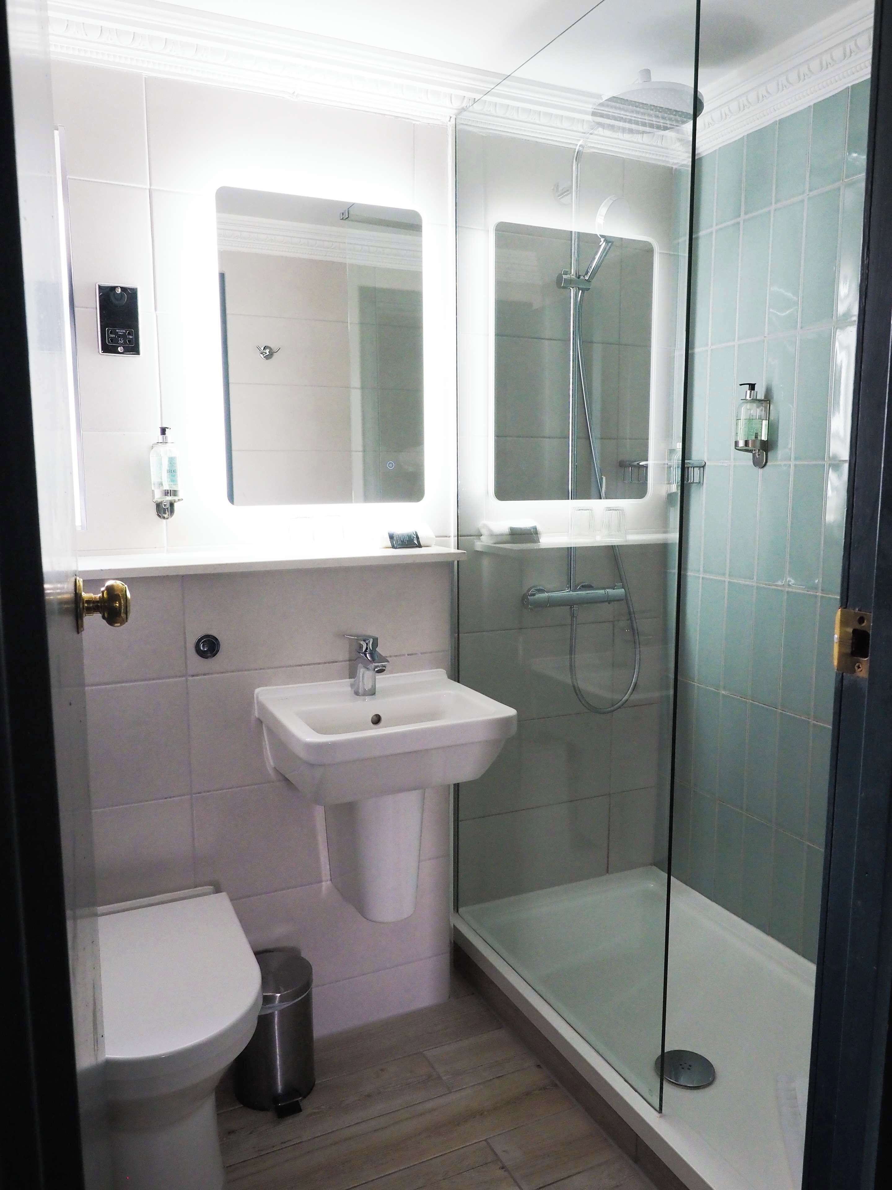 A bathroom with a white sink, a mirror, a glass-enclosed shower, and a toilet.
