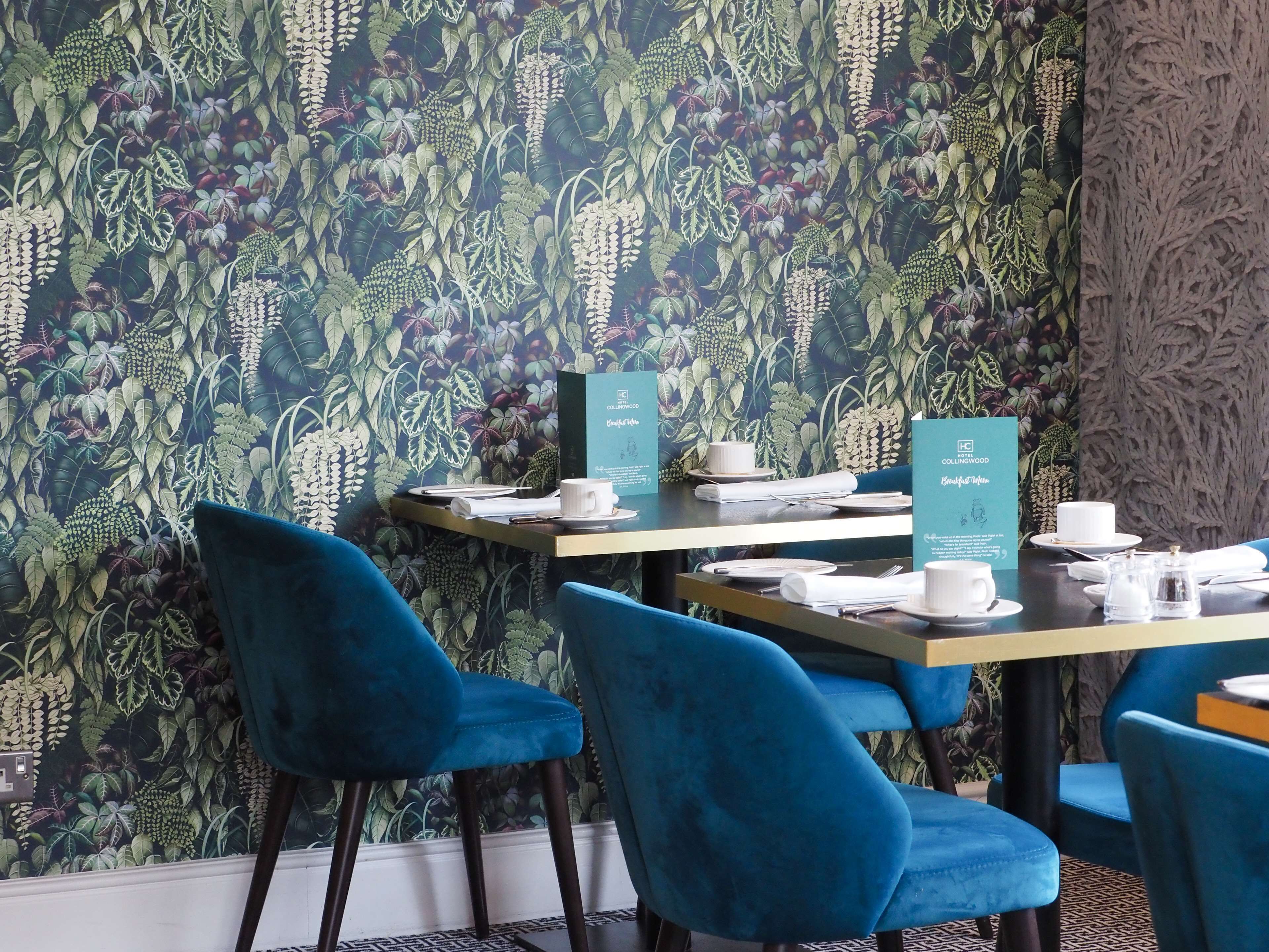 L’intérieur d’un restaurant, avec des chaises en velours bleu, des tables dressées avec des assiettes blanches, des tasses et des menus.