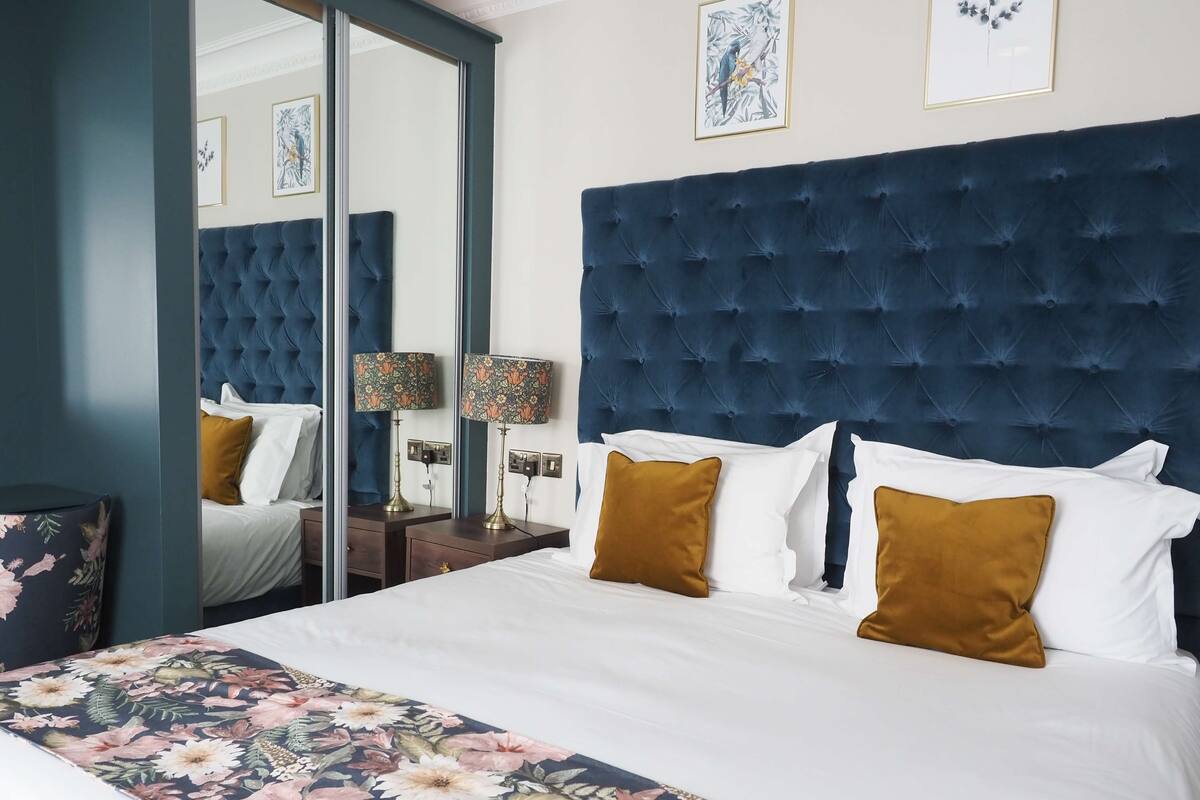 A hotel room with a large bed, a tufted headboard, floral bedding, and two bedside lamps.