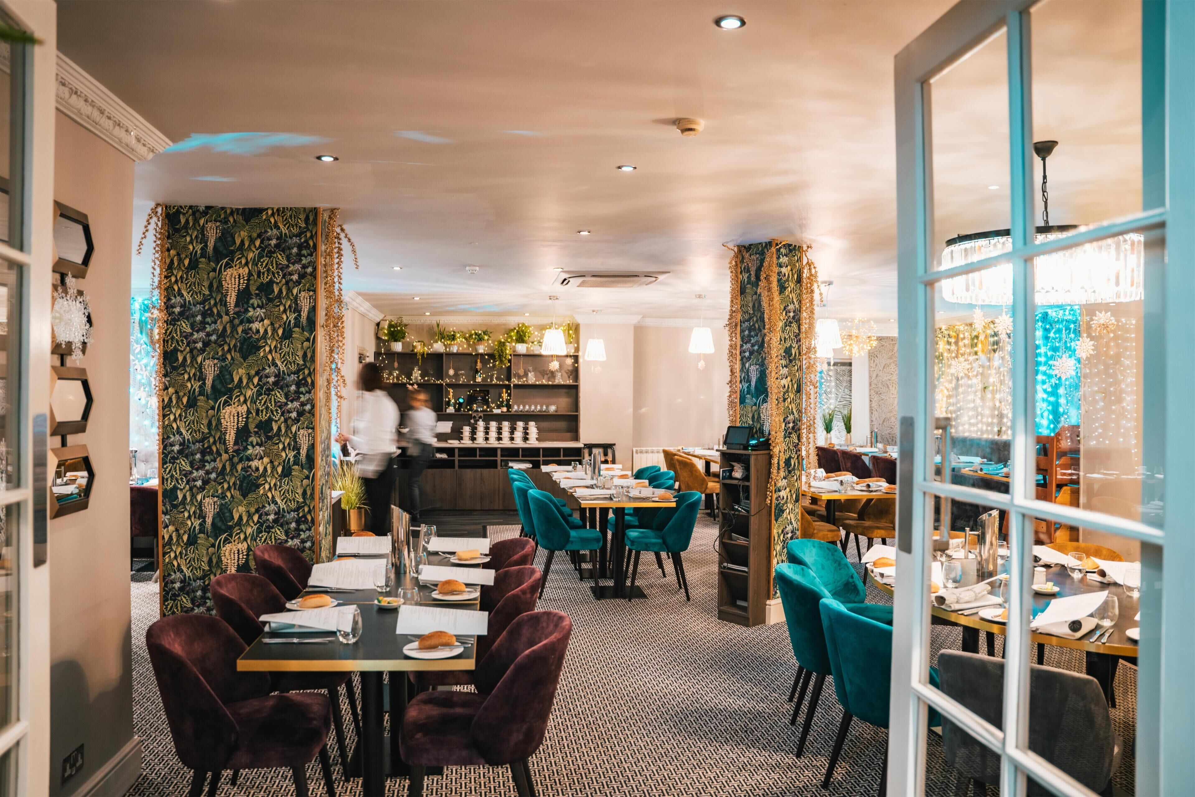 Um restaurante com parede estampada, cadeiras verde-água e um espaço de bar.