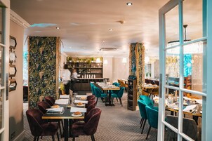 A restaurant with a patterned wall, teal chairs, and a bar area.