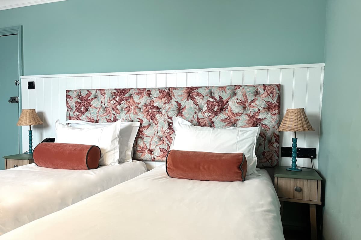 A double bed with white linens and two brown accent pillows, flanked by nightstands with lamps.