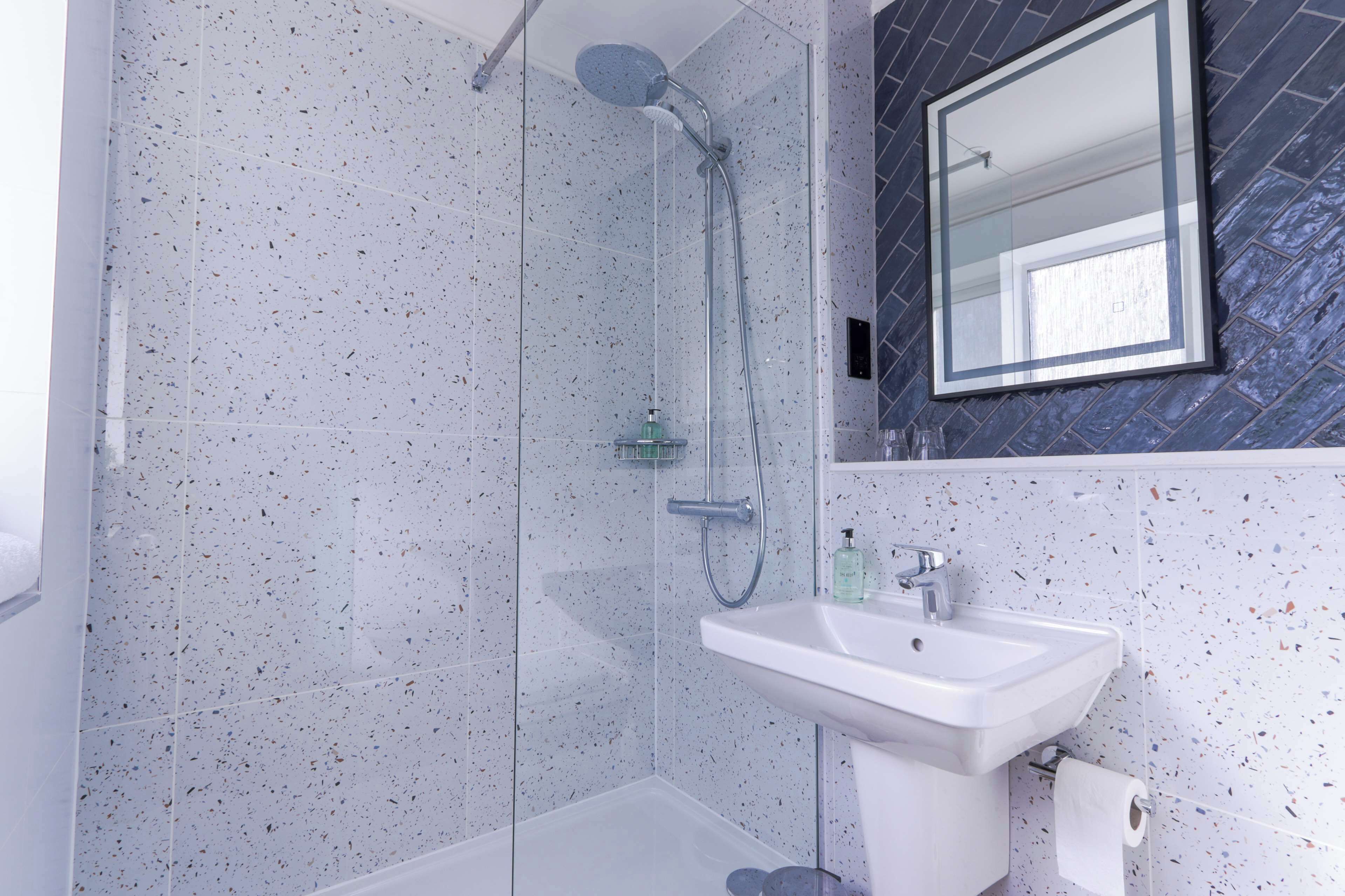 A modern bathroom with a glass-enclosed shower, a white sink, and a mirror with a dark backsplash.