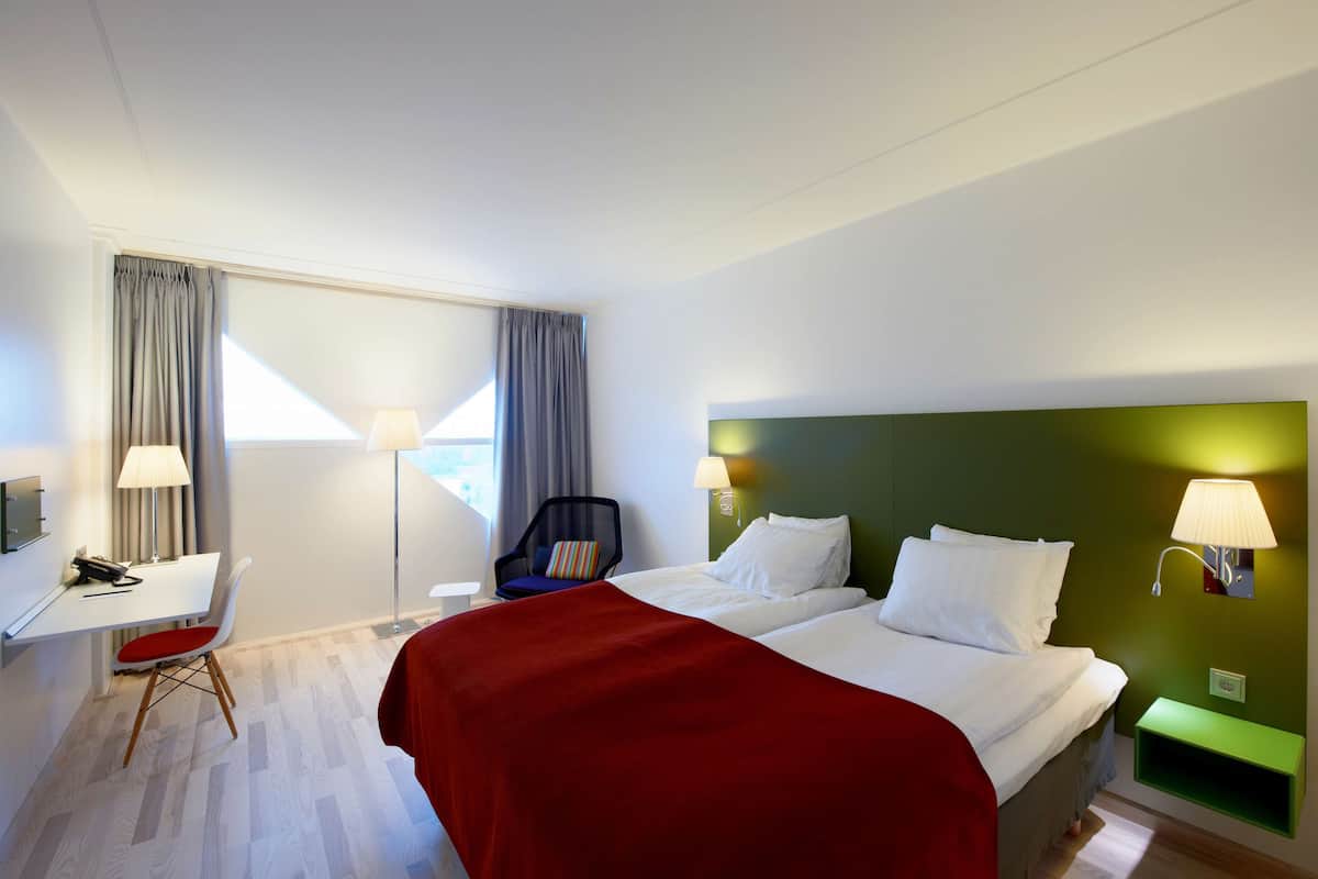 Habitació d'hotel amb llit, escriptori, cadira i tauleta de nit.