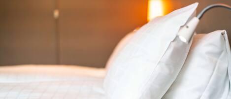 A neatly made bed with white bedding and pillows, a bedside lamp, and a wall-mounted light fixture.