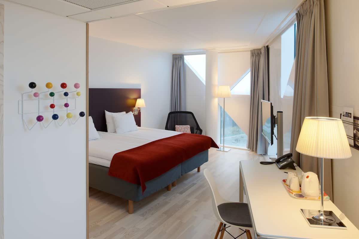 Una habitació d'hotel amb llit, escriptori, cadira i vista a l'exterior.