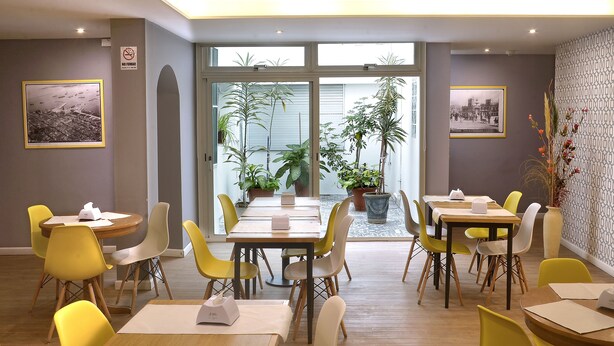 Un espace repas avec des chaises et des tables jaunes, des plantes en pot et des tableaux encadrés accrochés aux murs.