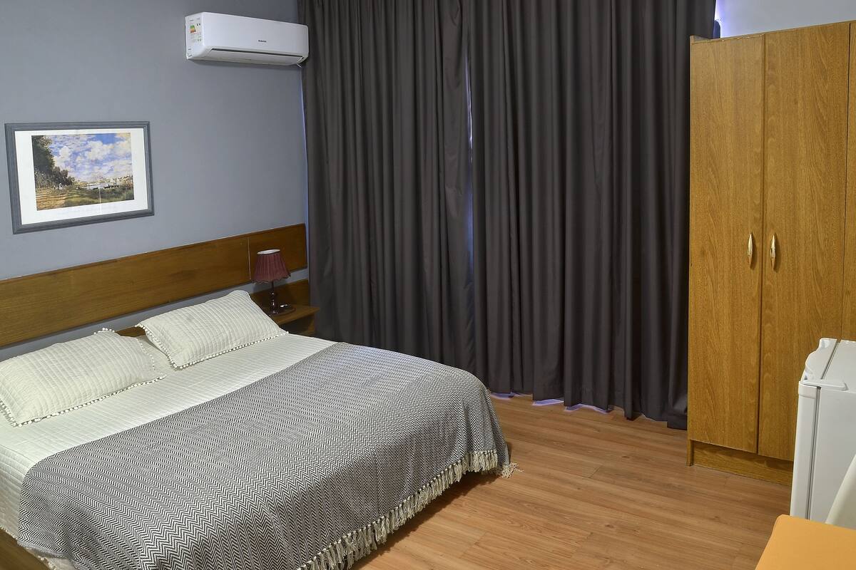 A bedroom with a bed, a wardrobe, a framed picture on the wall, and a window with curtains.