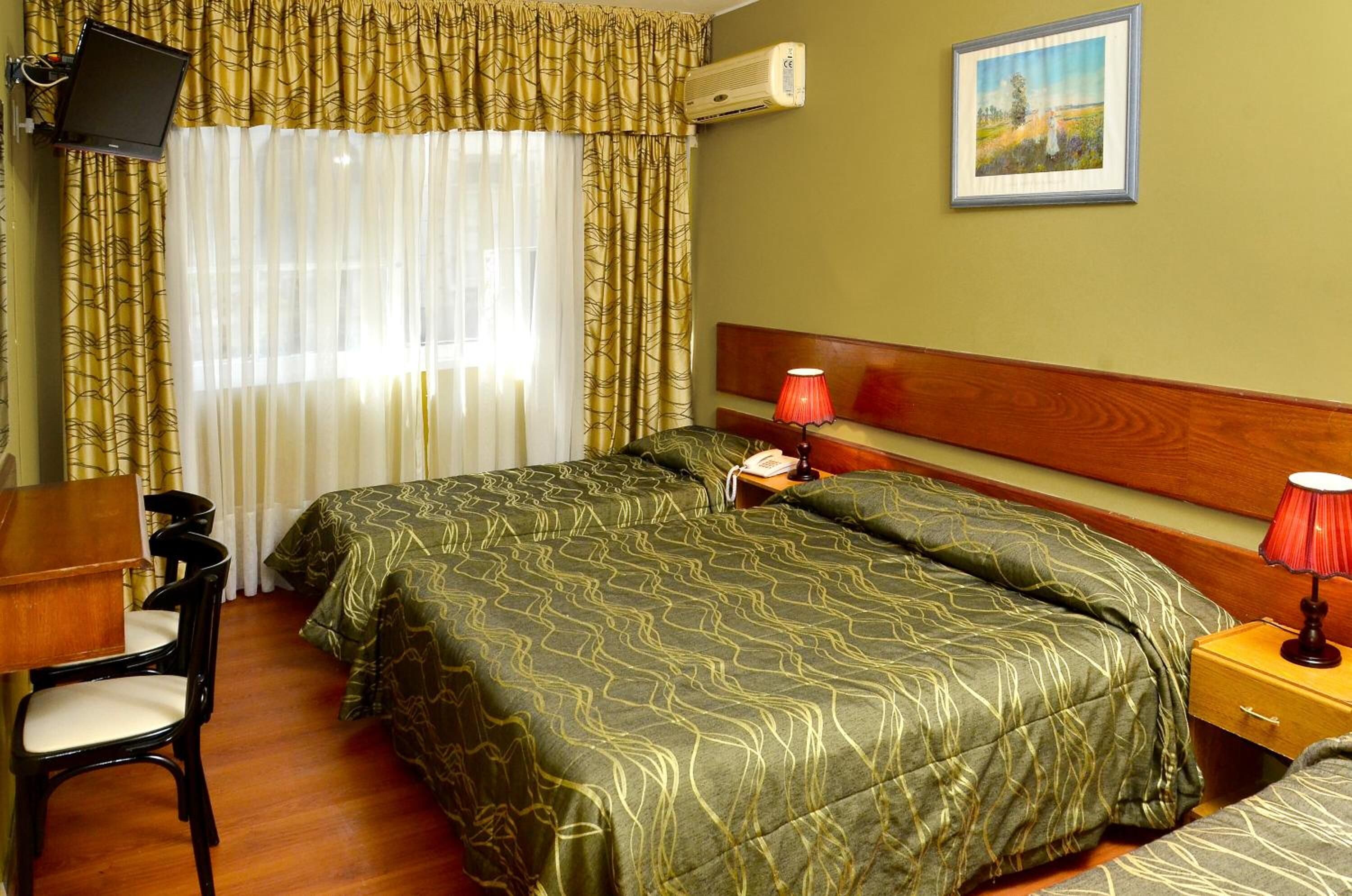 A hotel room with a bed, a desk, a chair, a nightstand with a lamp, and a picture on the wall.