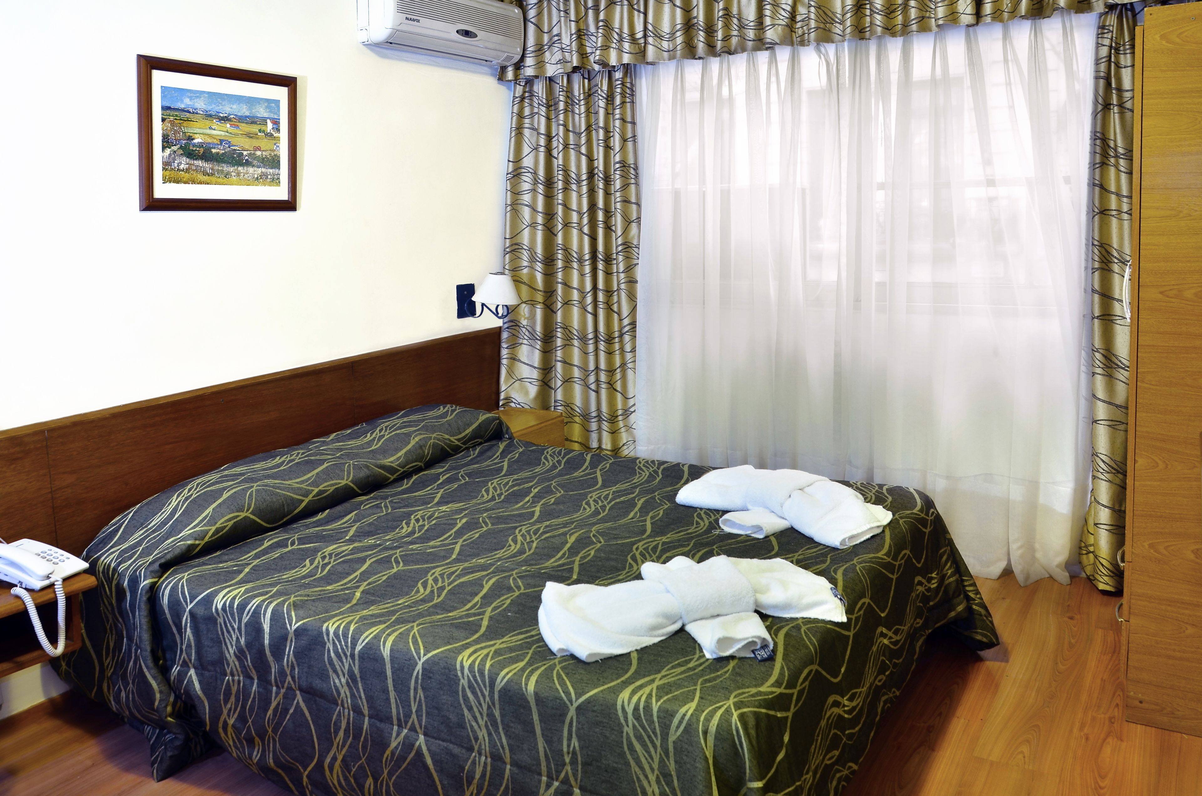 A hotel room with a bed, a bedside telephone, a lamp, and a painting on the wall.