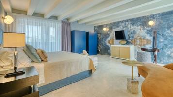 Una habitación de hotel moderna con una cama grande, un escritorio con lámpara, un televisor y un detalle de piedra en el suelo.