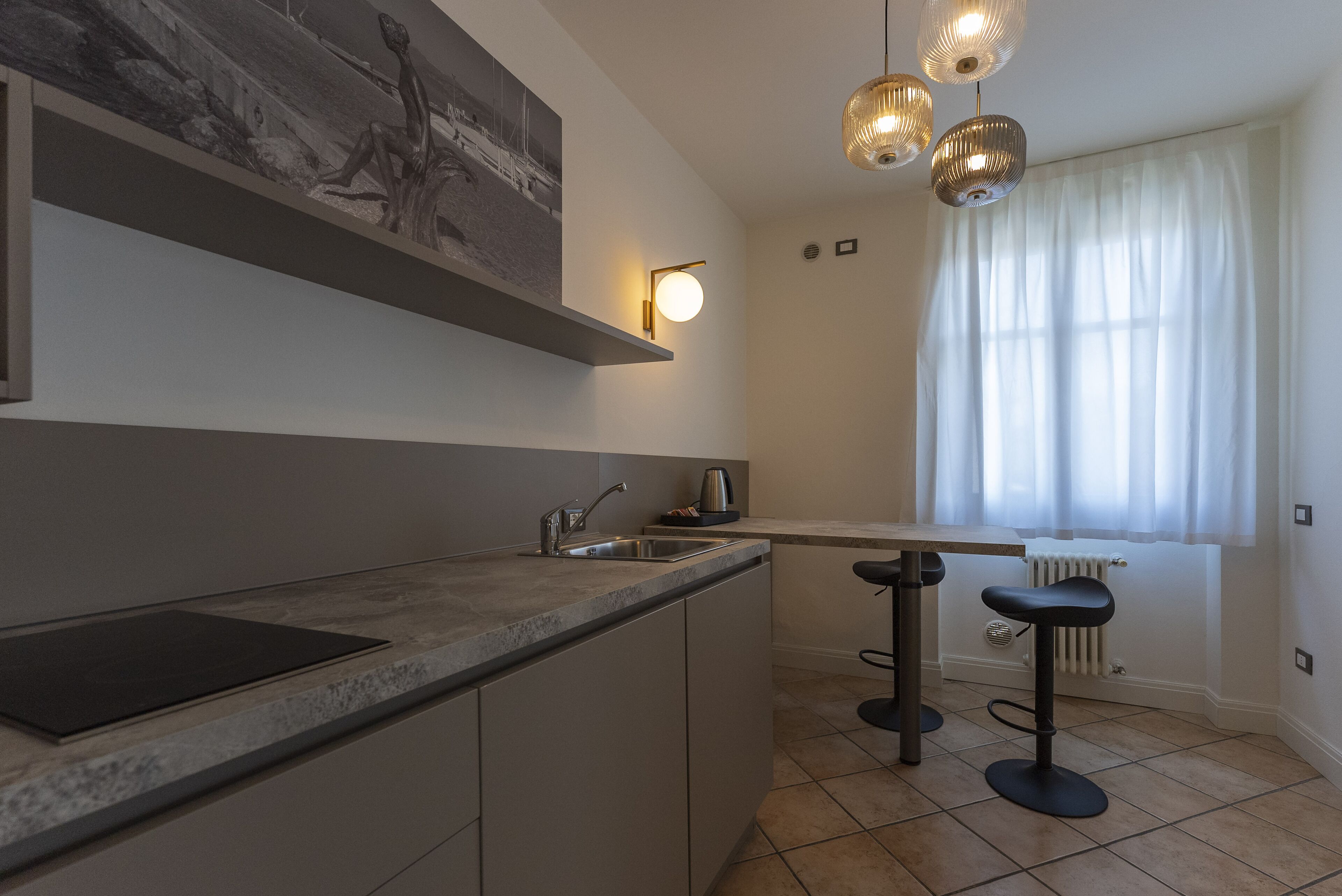 Una cucina moderna con isola integrata, illuminazione a sospensione e una finestra con tende leggere.