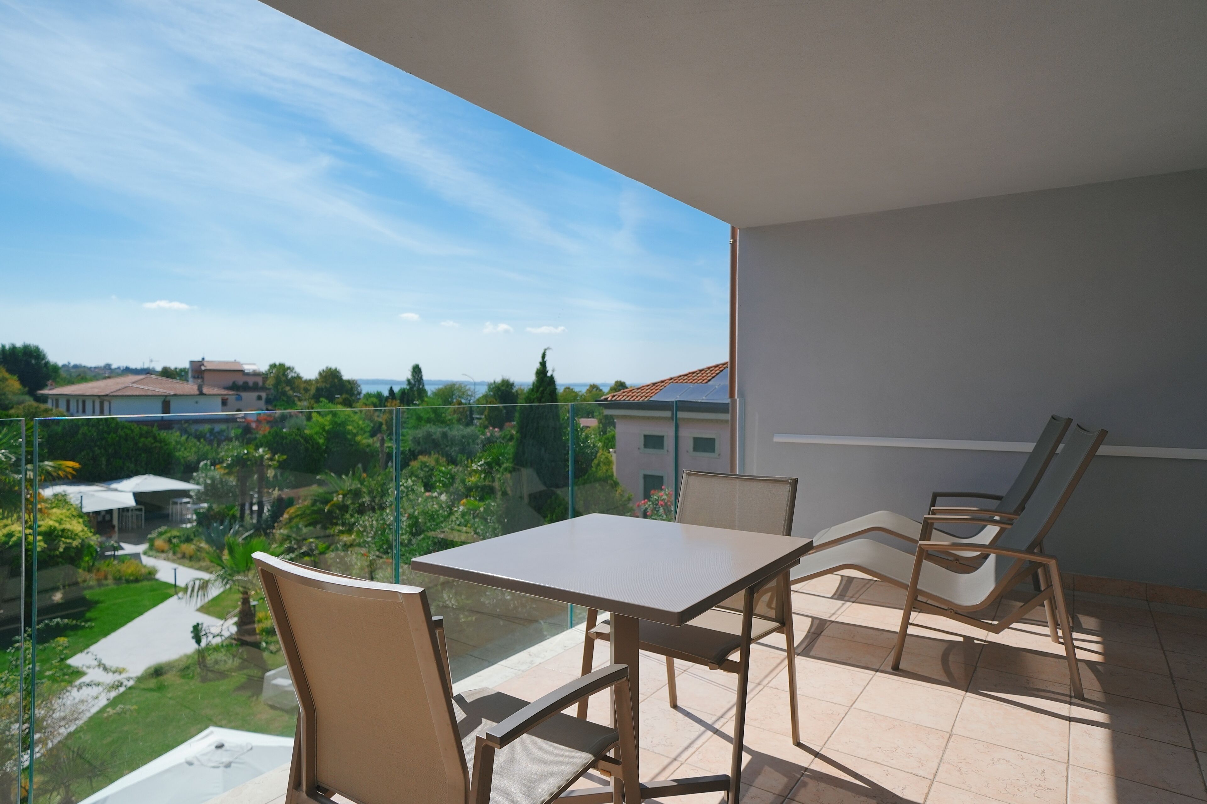 A balcony with a table and chairs, offering a view of a garden and buildings.