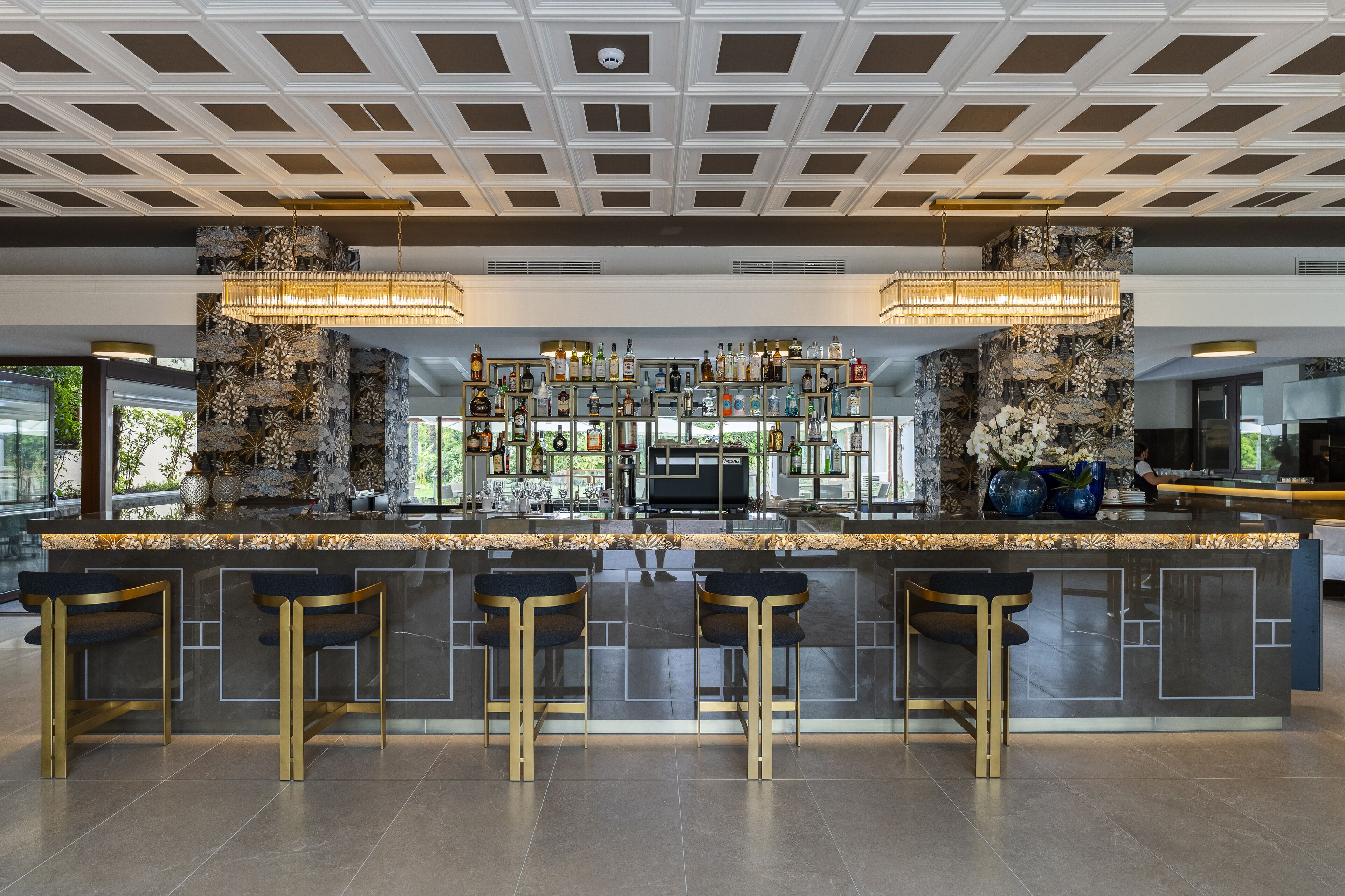 A modern bar area with a central island, bar stools, and a ceiling with a geometric pattern.
